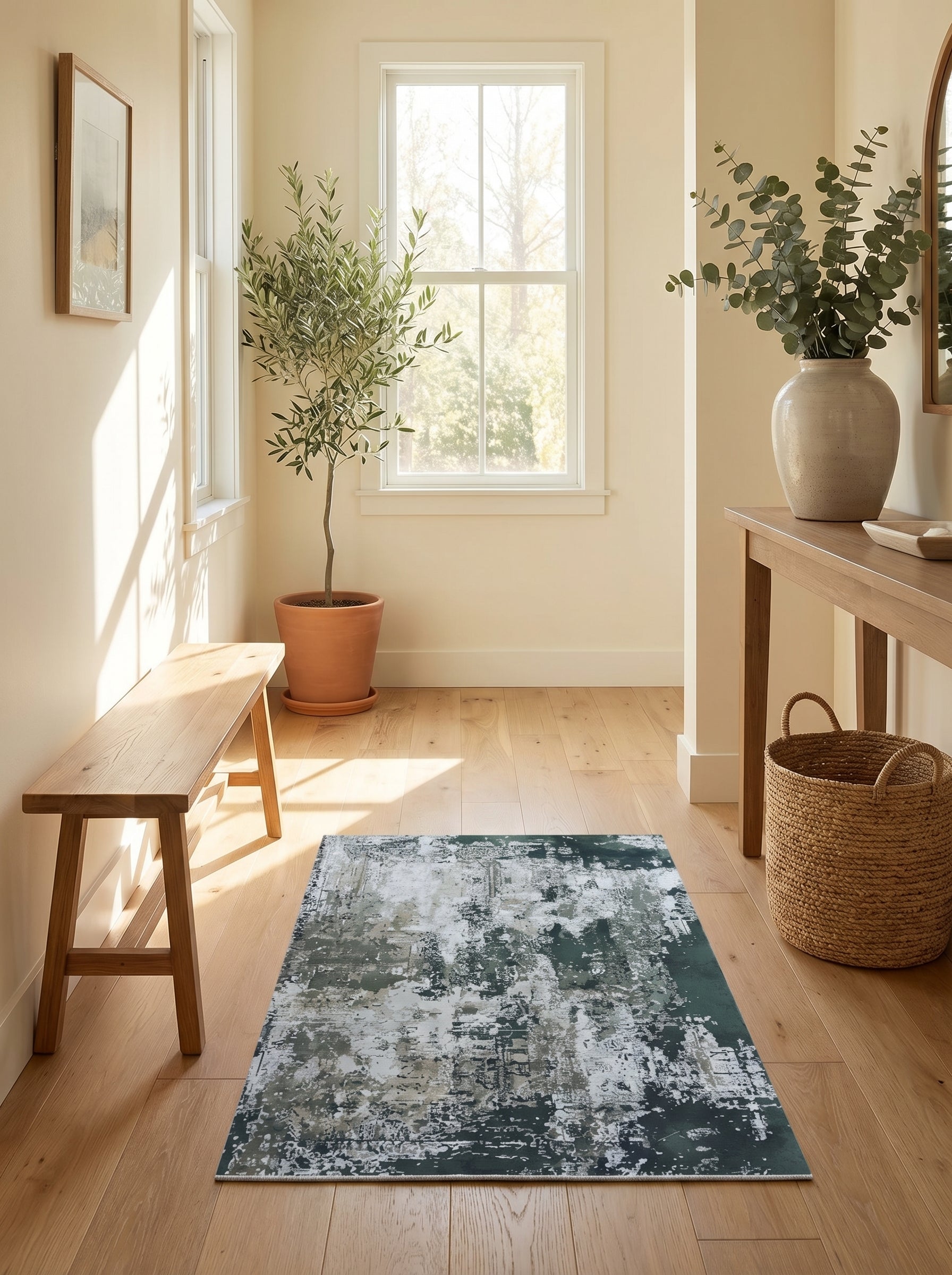 Tapis rectangulaire aux motifs abstraits et délavés verts foncés, gris, blancs et beiges, sur un parquet clair dans une entrée lumineuse