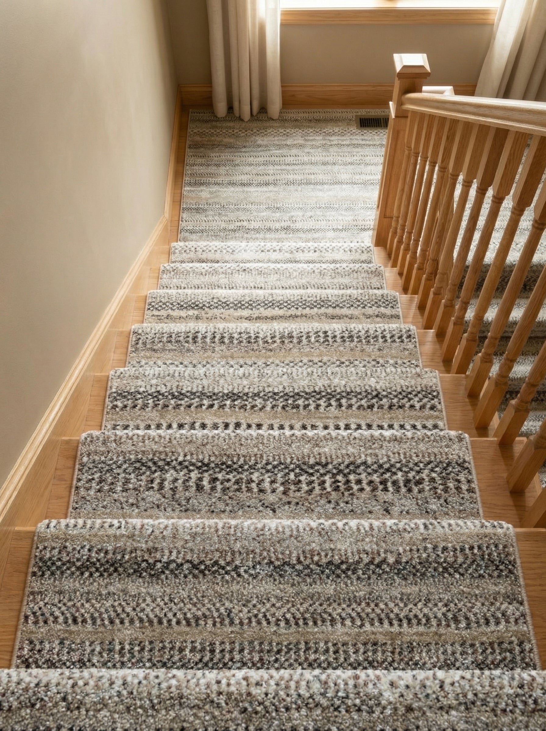 Tapis d'escalier en moquette, à motifs rayés et texturés beige, crème, gris et marron foncé, installée sur un escalier en bois clair