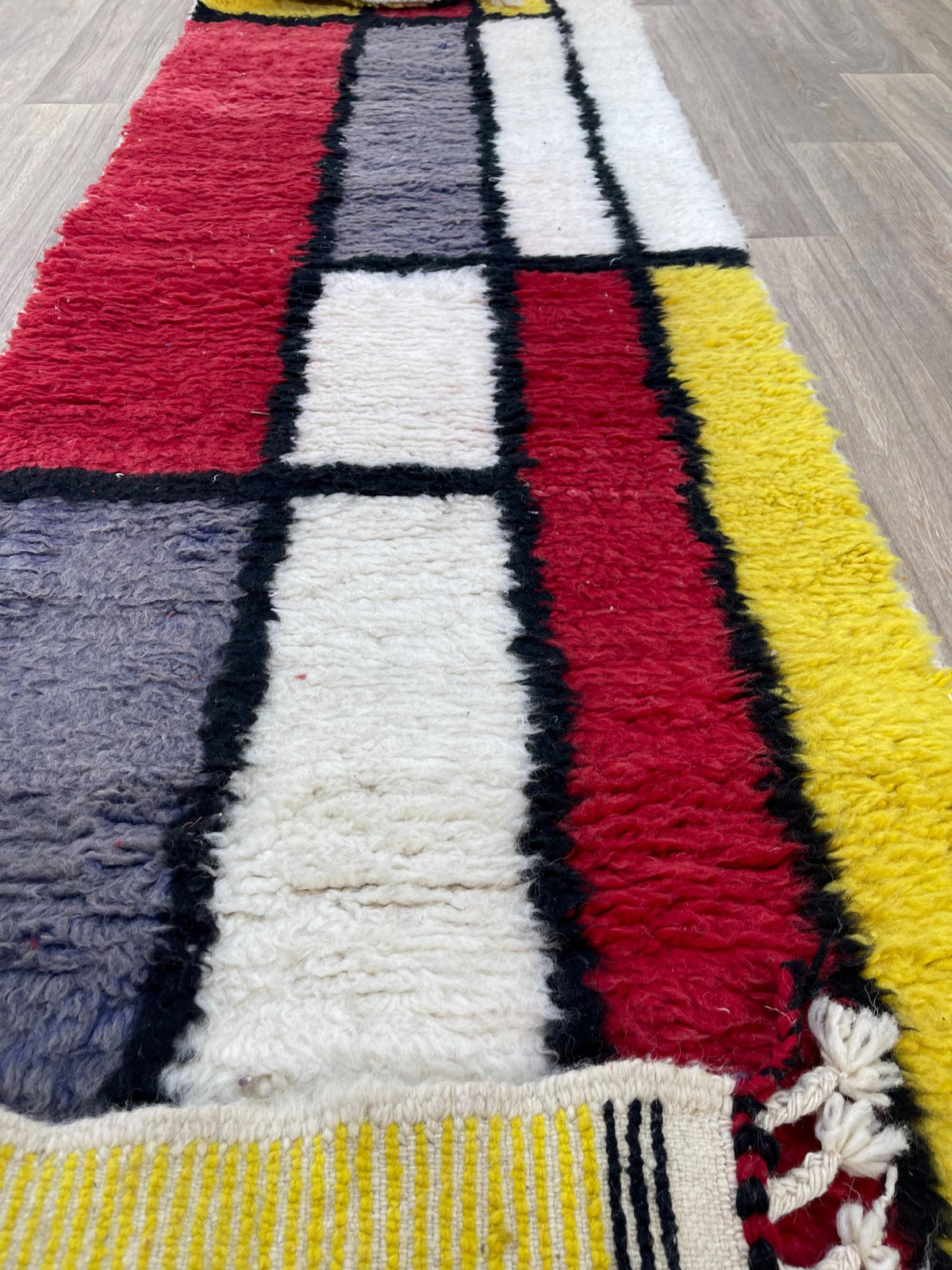 Gros plan sur un détail du tapis d'escalier berbère Azetta, poil long et motif rouge et jaune vus de près