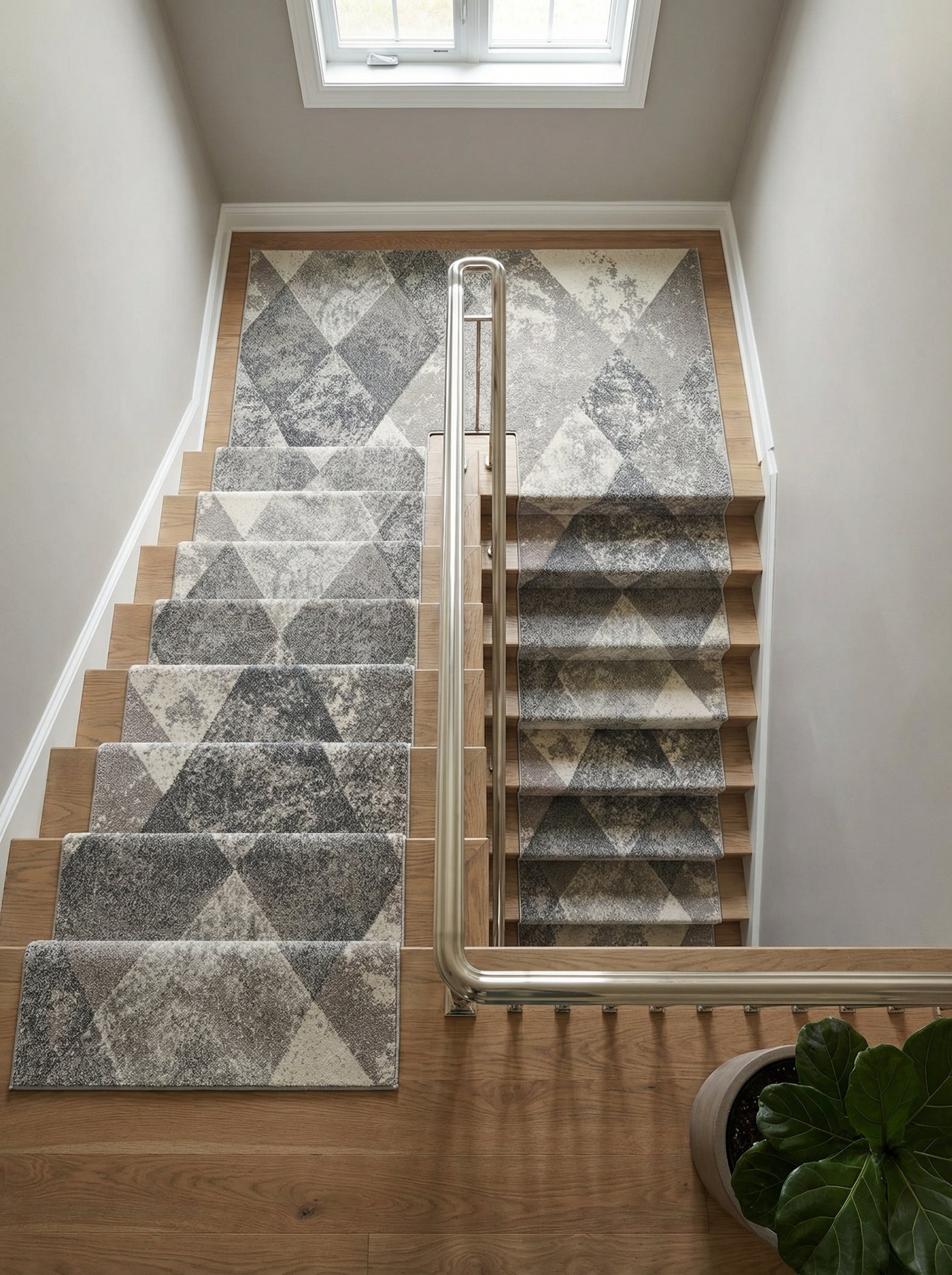 Tapis coureur texturé gris clair, foncé et blanc cassé, à motifs de losanges abstraits, habillant un escalier en bois et son palier lumineux