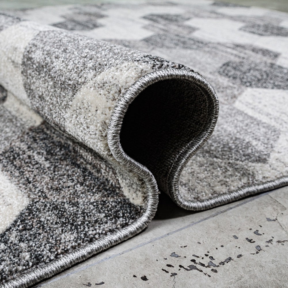 Un tapis texturé aux motifs abstraits gris foncé, gris clair et blanc cassé est partiellement roulé