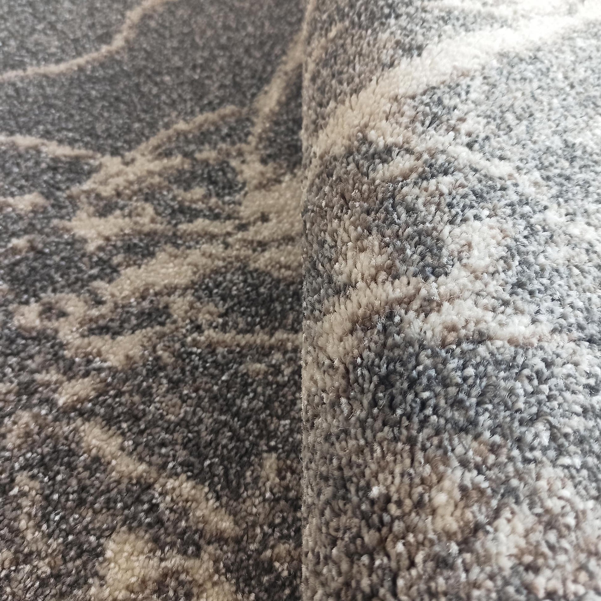 Gros plan sur un tapis enroulé, aux fibres épaisses et à la texture douce, mêlant des motifs ondulés gris et beiges