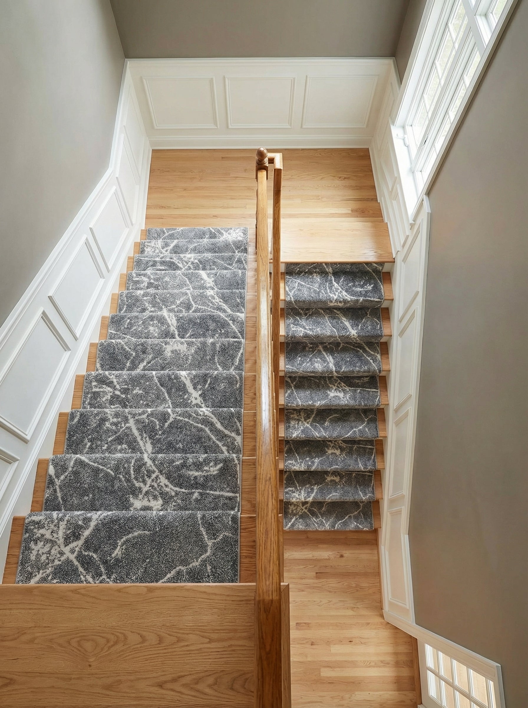 Tapis d'escalier gris anthracite chiné à motifs abstraits blancs évoquant le marbre, sur marches en bois clair, dans un hall d'entrée