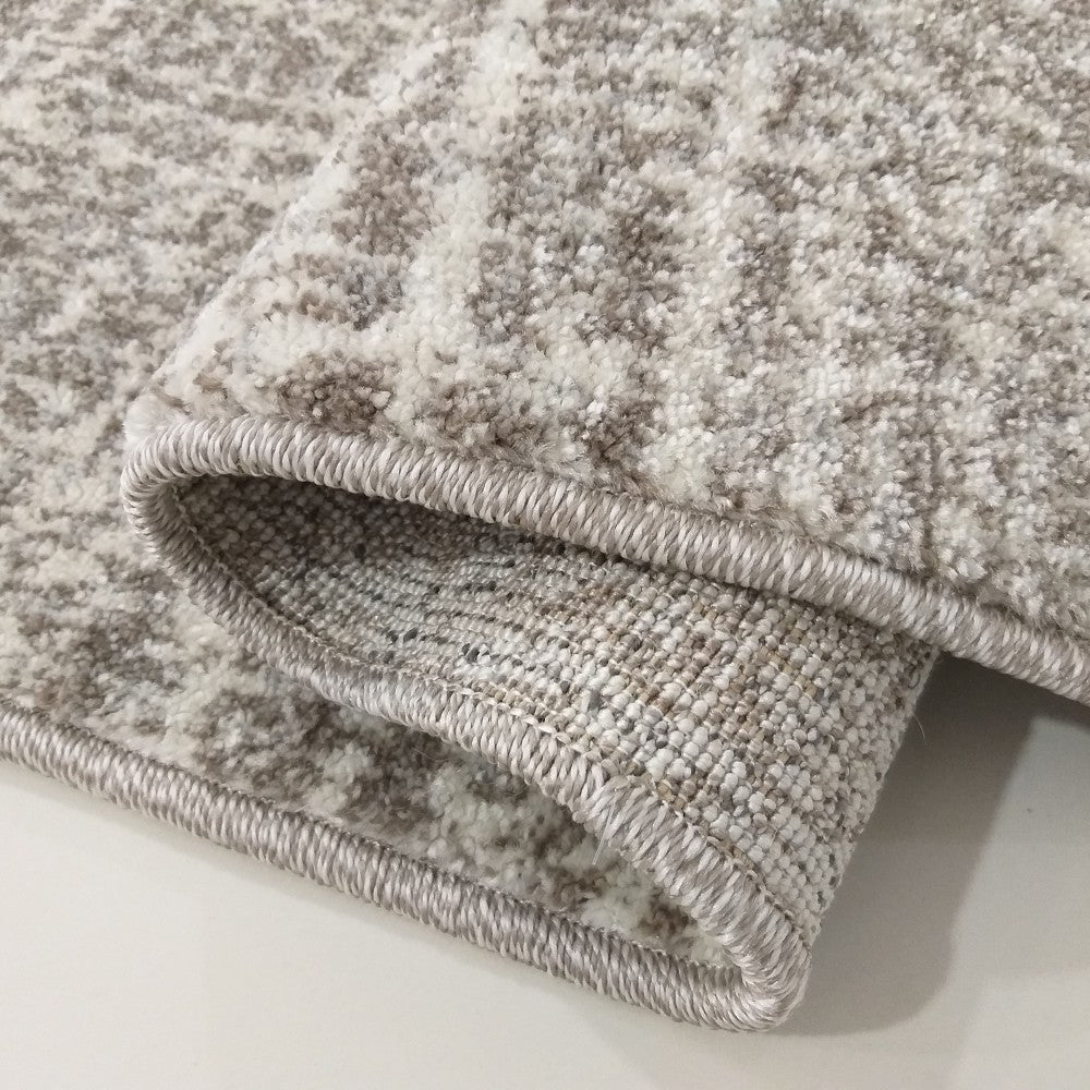 Tapis doux aux tons crème et beige avec un motif moucheté, montrant sa surface bouclée et son bord ourlé