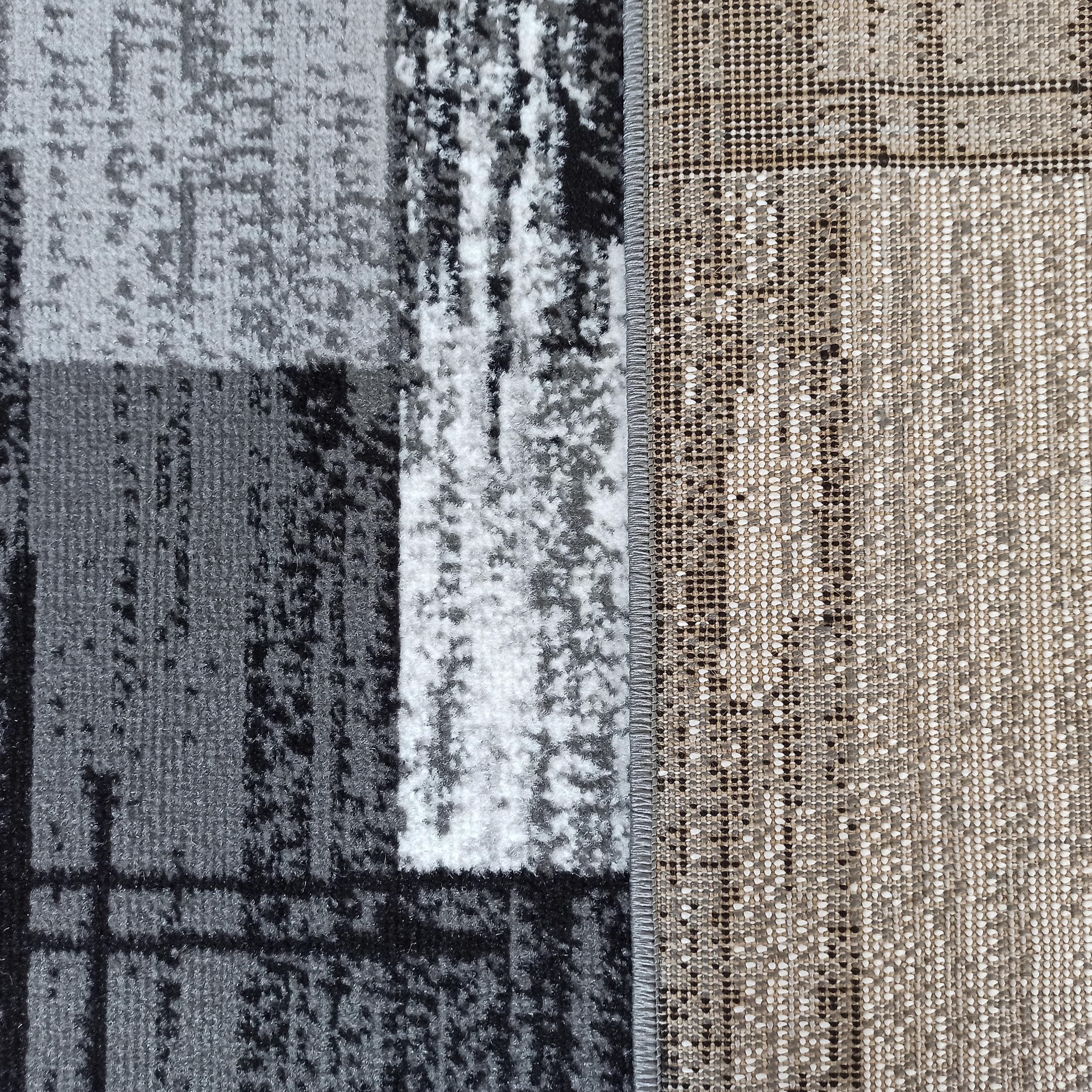 Tapis avec une surface à poils courts gris, noirs et blancs à motif abstrait, et un envers tissé beige et marron