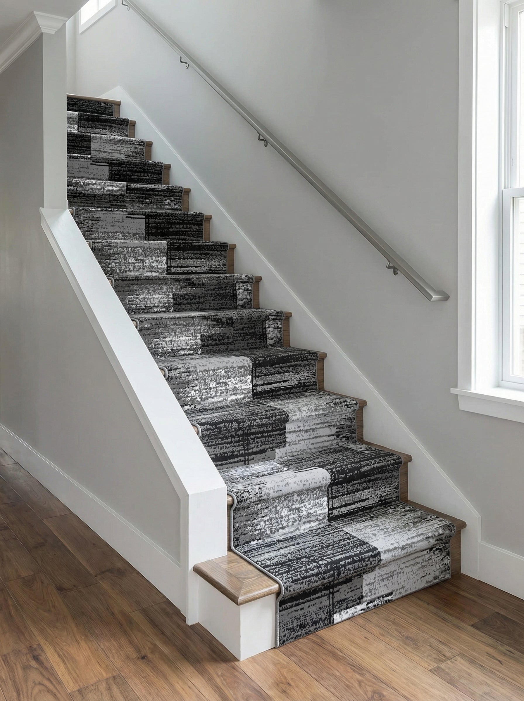 Tapis d'escalier textile aux motifs abstraits noirs, gris et blancs, formant un patchwork moderne dans une cage d'escalier lumineuse
