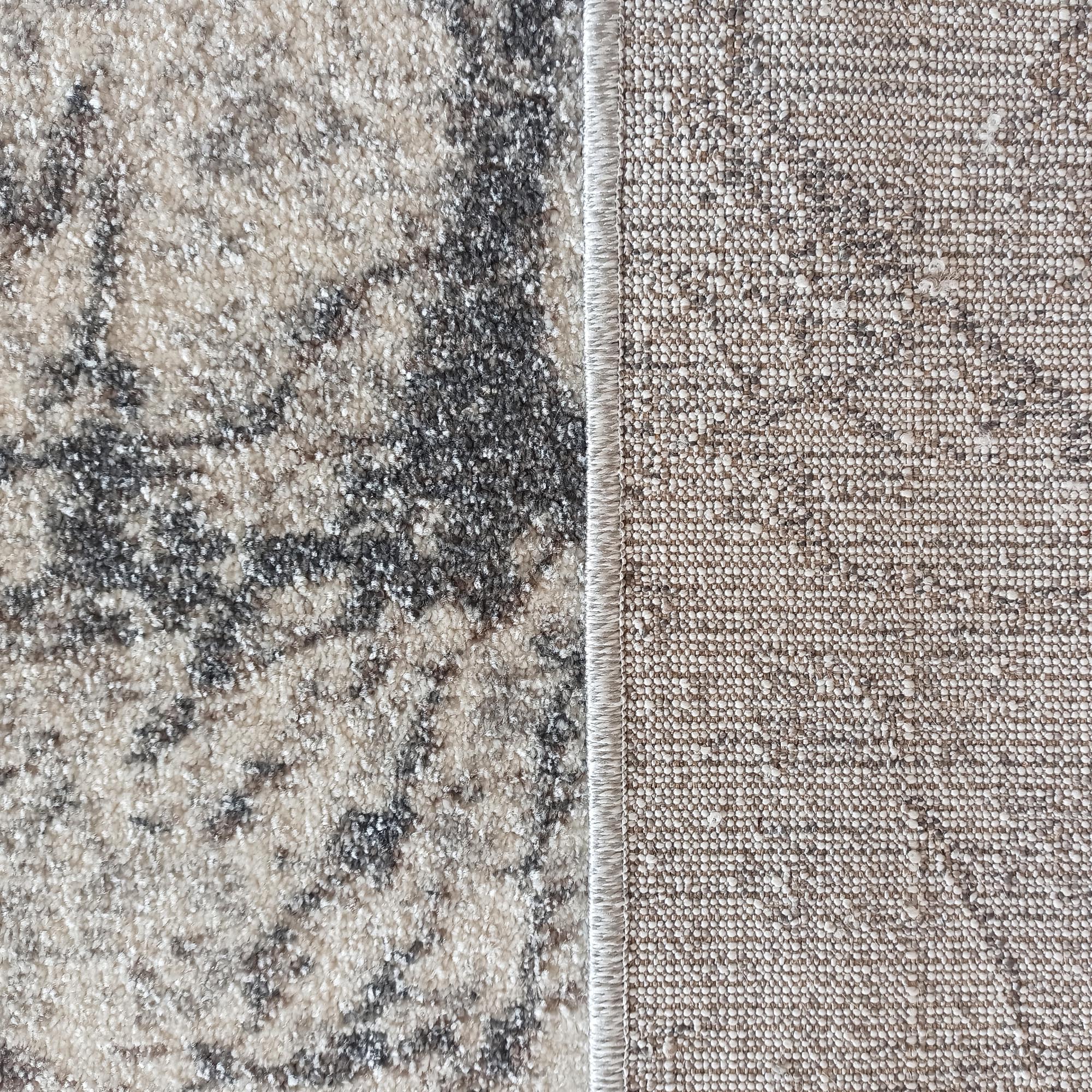 Tapis présentant sa surface à motif abstrait gris foncé et beige texturé et son envers en tissage serré beige