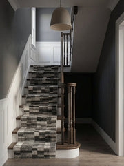 Tapis d'escalier à motifs de blocs rectangulaires gris, noirs et blancs, installés sur un escalier en bois d'une entrée