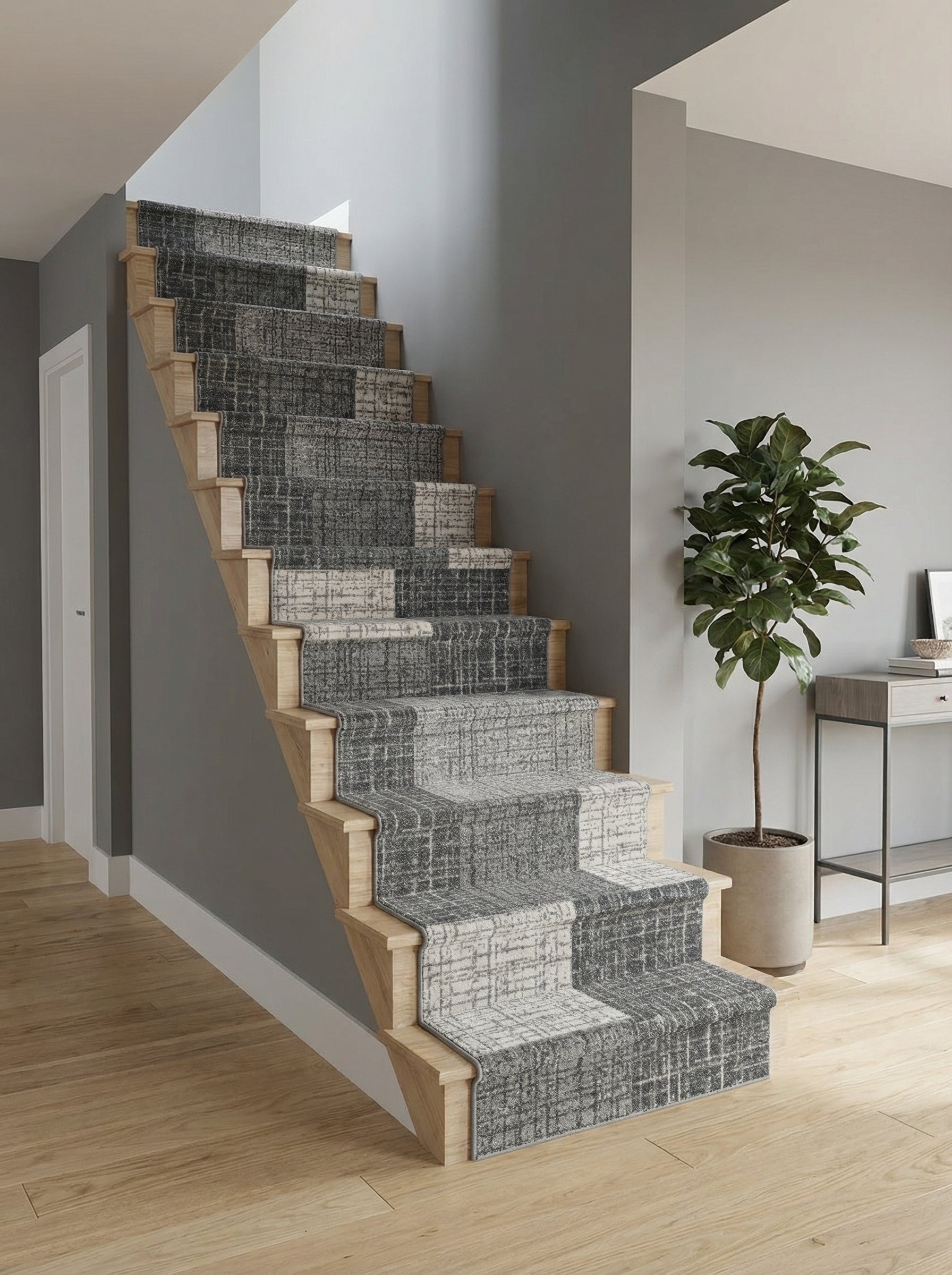 Tapis d'escalier à motifs géométriques gris foncé et blanc cassé, posé sur des marches en bois clair dans une entrée moderne