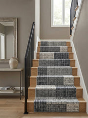 Tapis d'escalier gris anthracite et gris clair, à motifs abstraits et texturés formant des blocs, sur des marches en bois clair dans une entrée