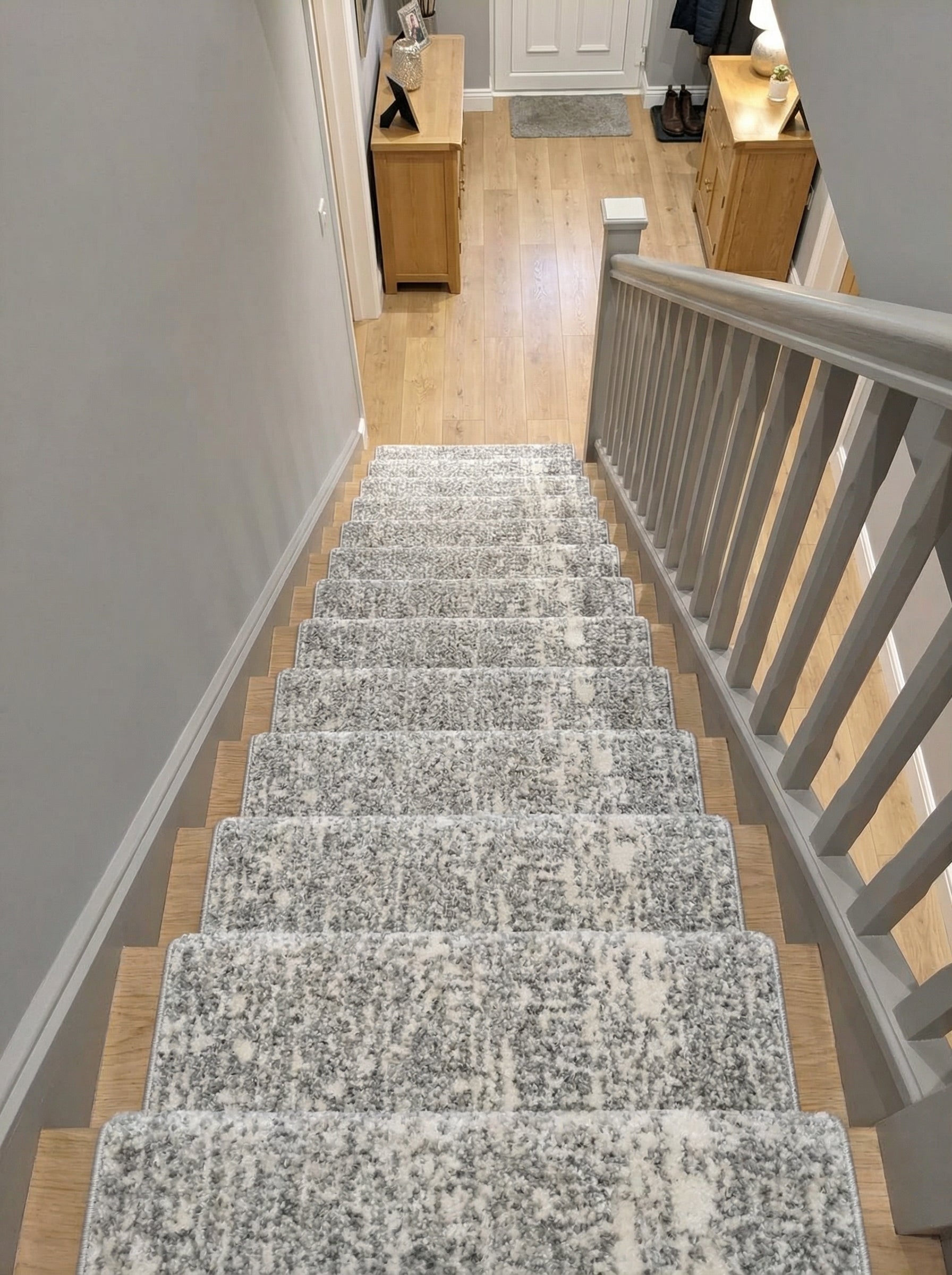 Tapis d'escalier en moquette grise et blanche à motifs mouchetés, recouvrant les marches d'un escalier menant à une entrée