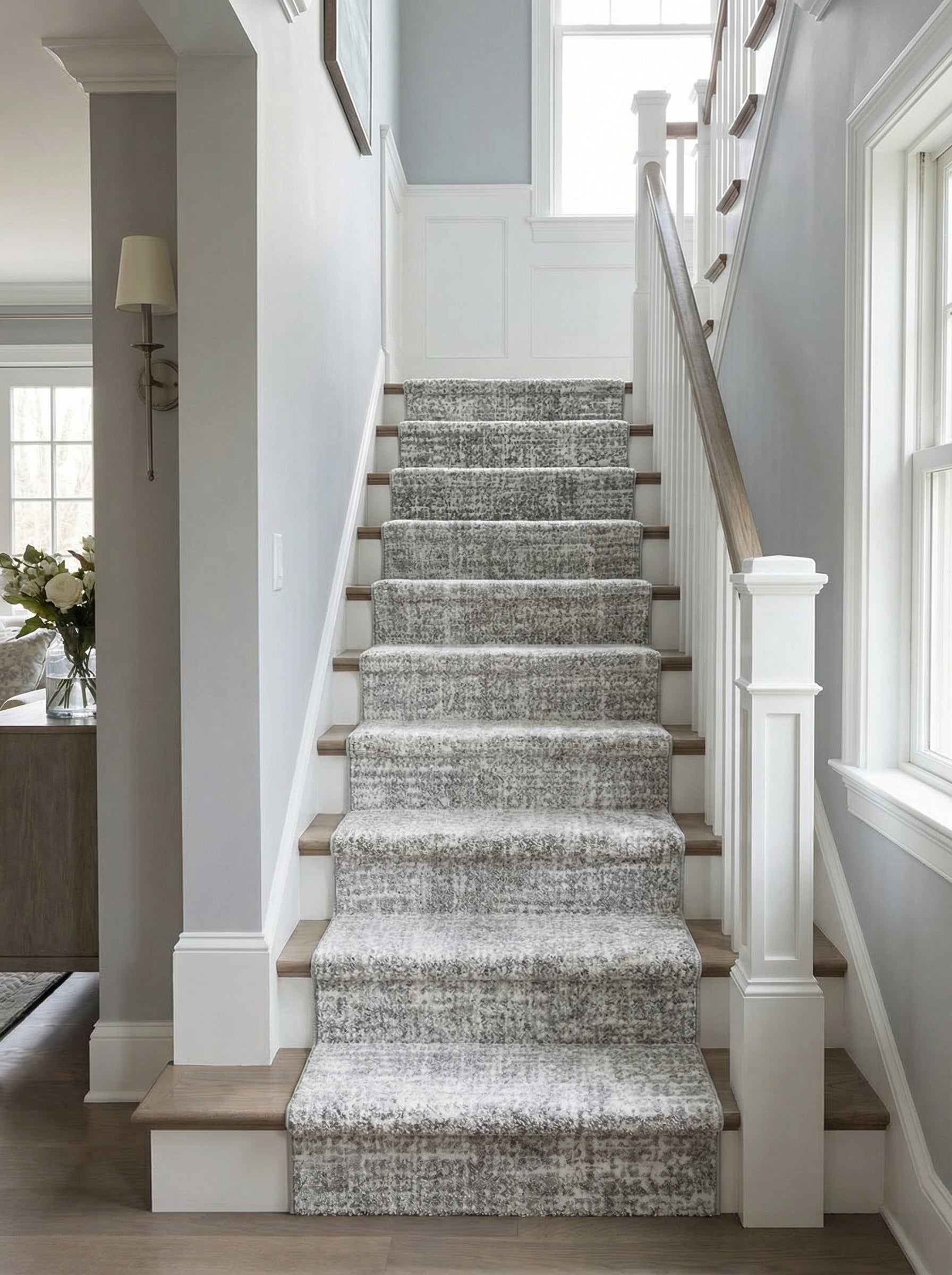 Tapis d'escalier gris et blanc à motifs abstraits et texture épaisse, posé sur des marches en bois clair dans un hall d'entrée élégant