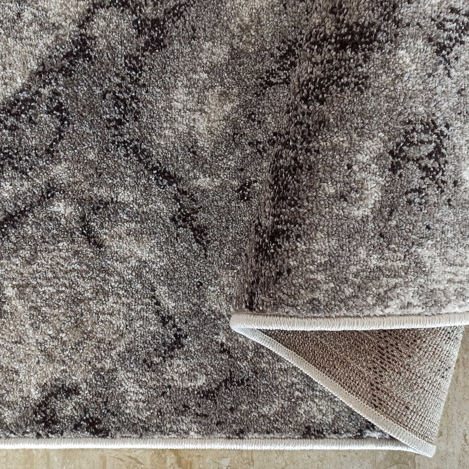 Tapis moelleux aux motifs abstraits gris, noirs et blancs, un coin relevé sur son dos tissé et sa bordure crème