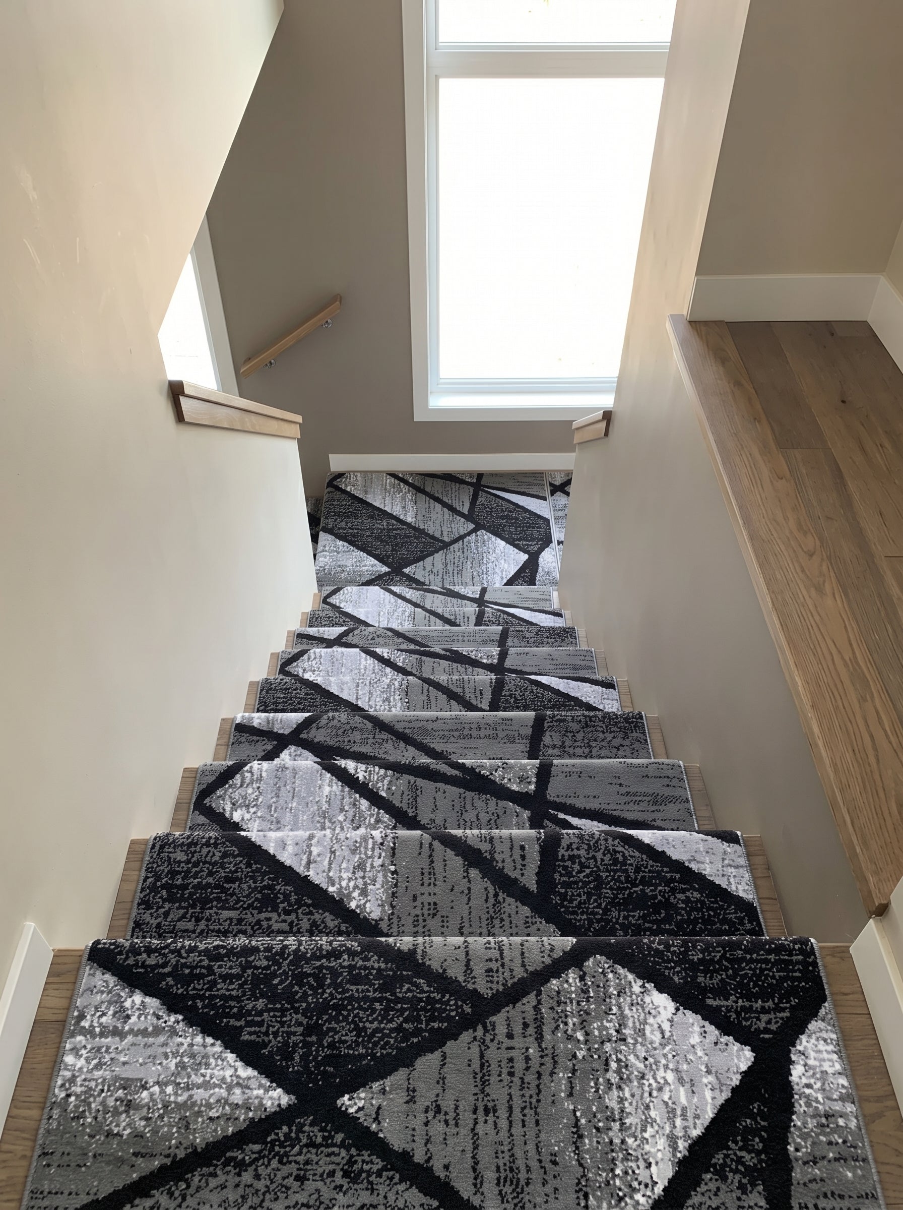 Tapis d'escalier moderne, gris et noir avec des motifs géométriques abstraits, installé dans une cage d'escalier lumineuse