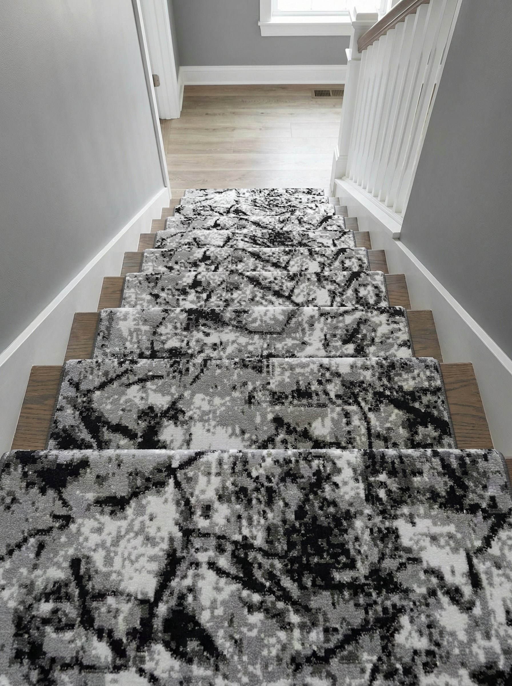 Tapis d'escalier à motifs abstraits noirs, gris et blancs sur des marches en bois, dans une entrée