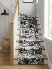 Un tapis d'escalier à motif abstrait gris, noir et blanc, posé sur des marches en bois clair dans une entrée lumineuse
