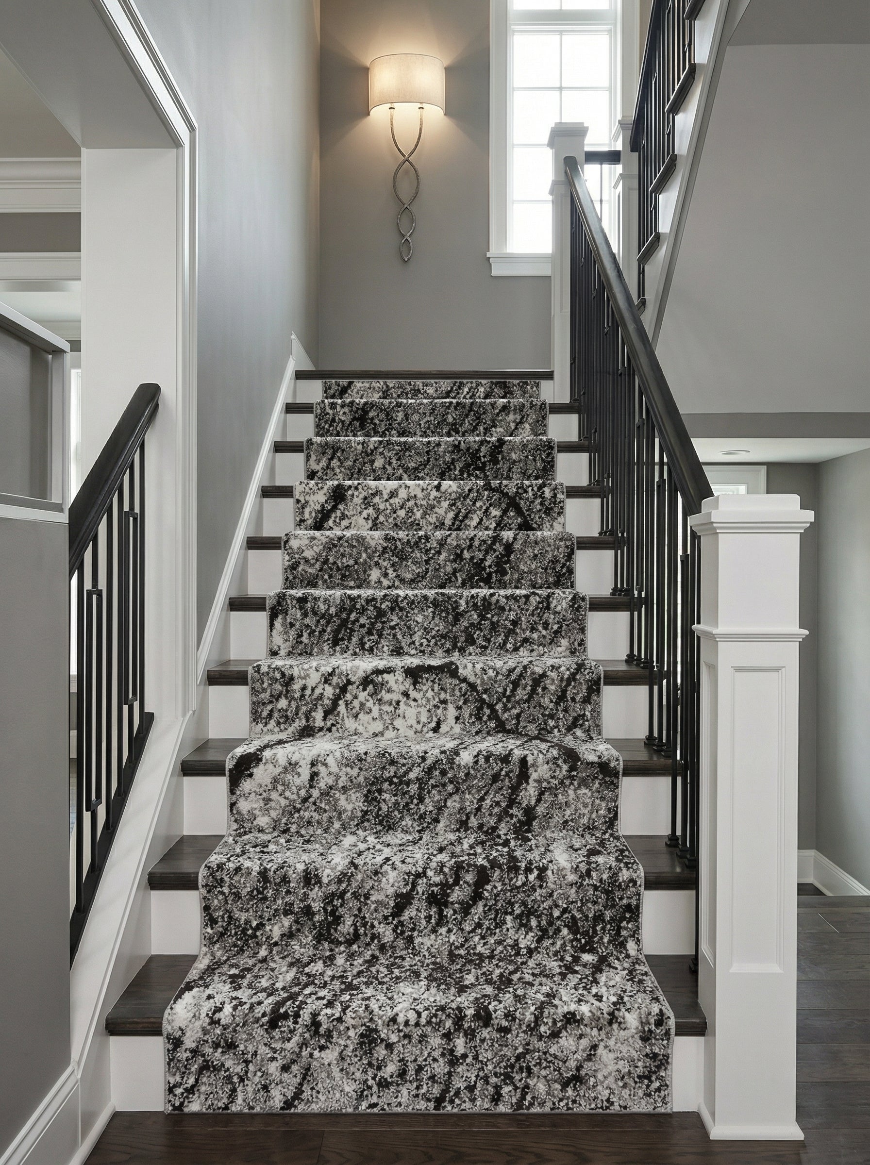 Tapis d'escalier noir, blanc et gris aux motifs abstraits et mouchetés, installé sur des marches en bois dans un hall d'entrée