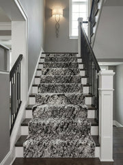 Tapis d'escalier noir, blanc et gris aux motifs abstraits et mouchetés, installé sur des marches en bois dans un hall d'entrée