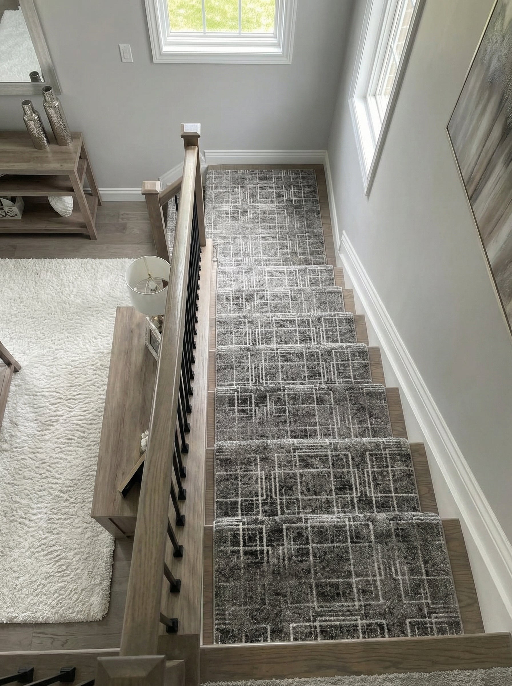 Tapis d'escalier gris aux motifs géométriques abstraits de lignes et carrés blancs, recouvrant des marches en bois dans un hall d'entrée