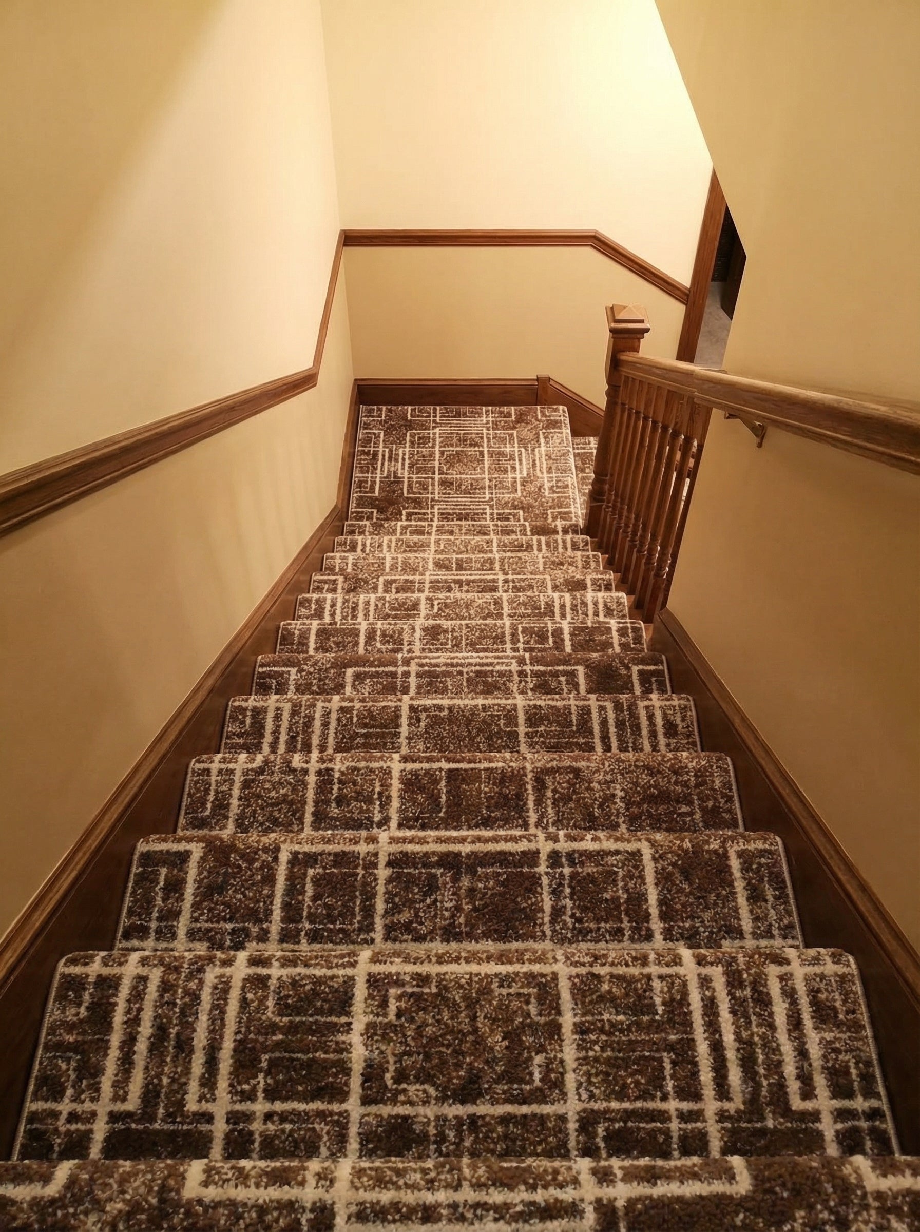 Long tapis d'escalier marron chiné et crème à motifs géométriques, posé sur des marches en bois, dans une cage d'escalier