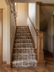 Tapis d'escalier marron foncé aux motifs géométriques blancs et texturés sur des marches en bois dans une entrée