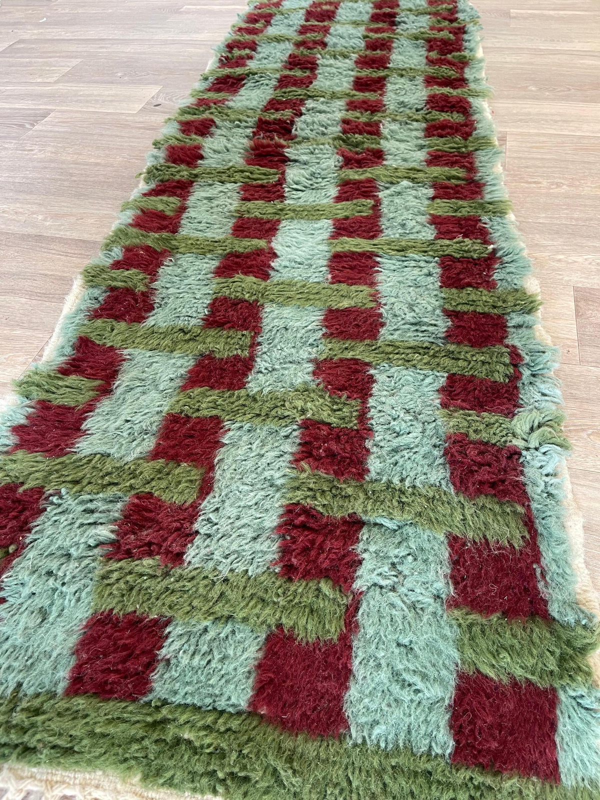 Gros plan sur un détail du tapis de couloir berbère Oualidia, poil long et motif vert et bordeaux vus de près