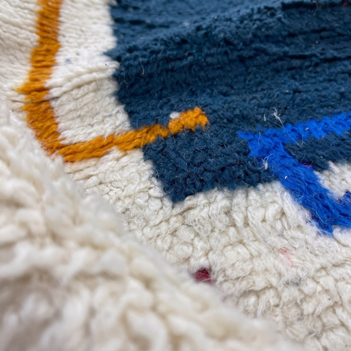 Gros plan sur un motif du tapis de couloir berbère Bouregreg, couloir écru à poil long, liseré marine