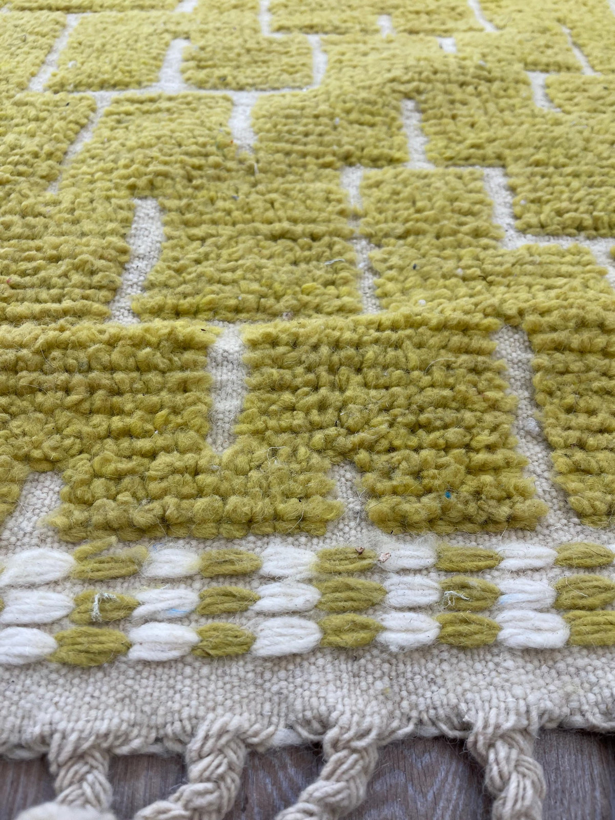 Gros plan sur les franges du tapis de couloir berbère Timzin, écrues tressées à pompons en bas, nouées à la main