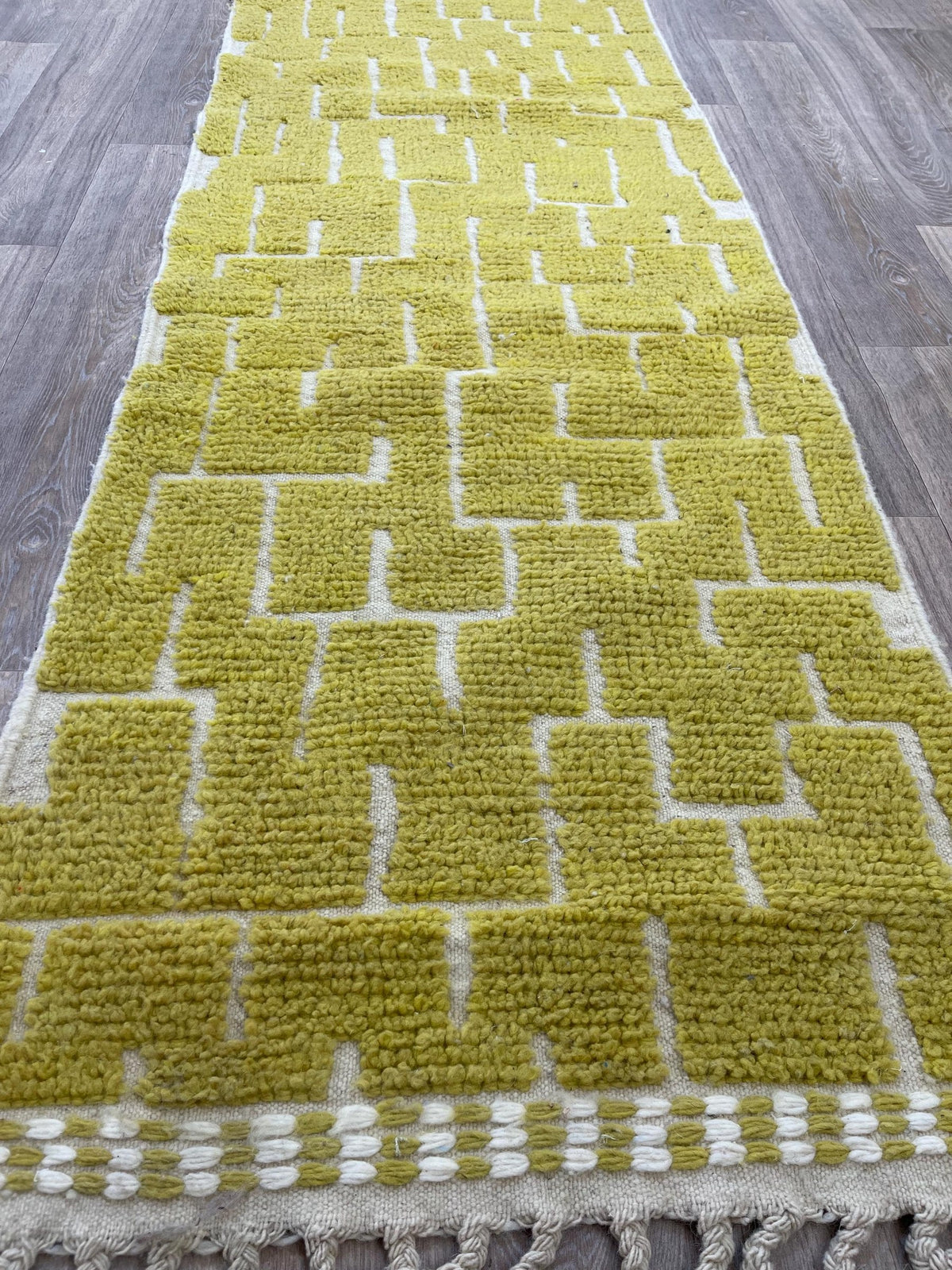 Gros plan sur un détail du tapis de couloir berbère Timzin, poil ras et motif jaune moutarde vus de près