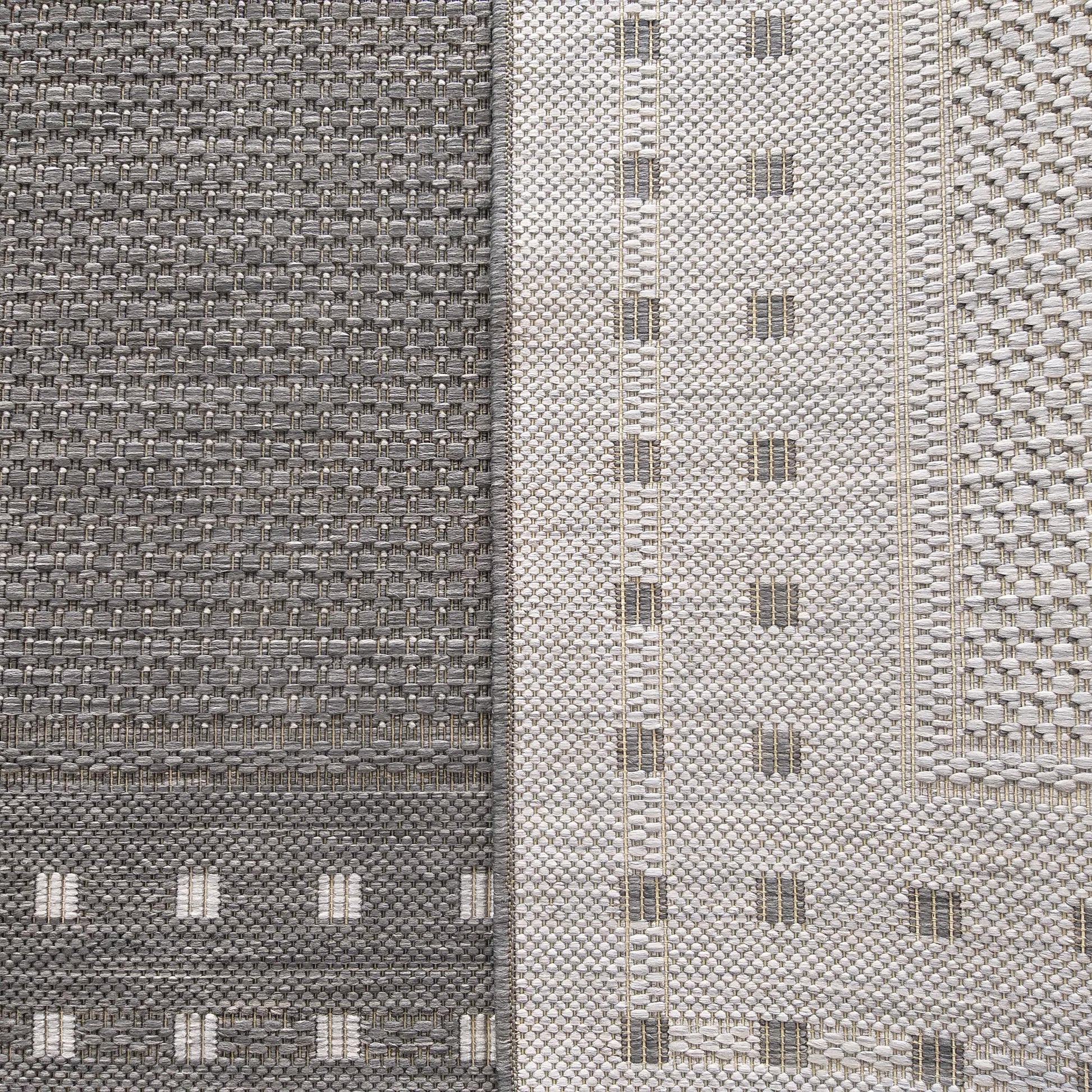 Tapis bicolore en tissage texturé. Une moitié gris foncé avec des carrés clairs, l'autre gris clair avec des lignes sombres, le tout entrelacé de fils beiges
