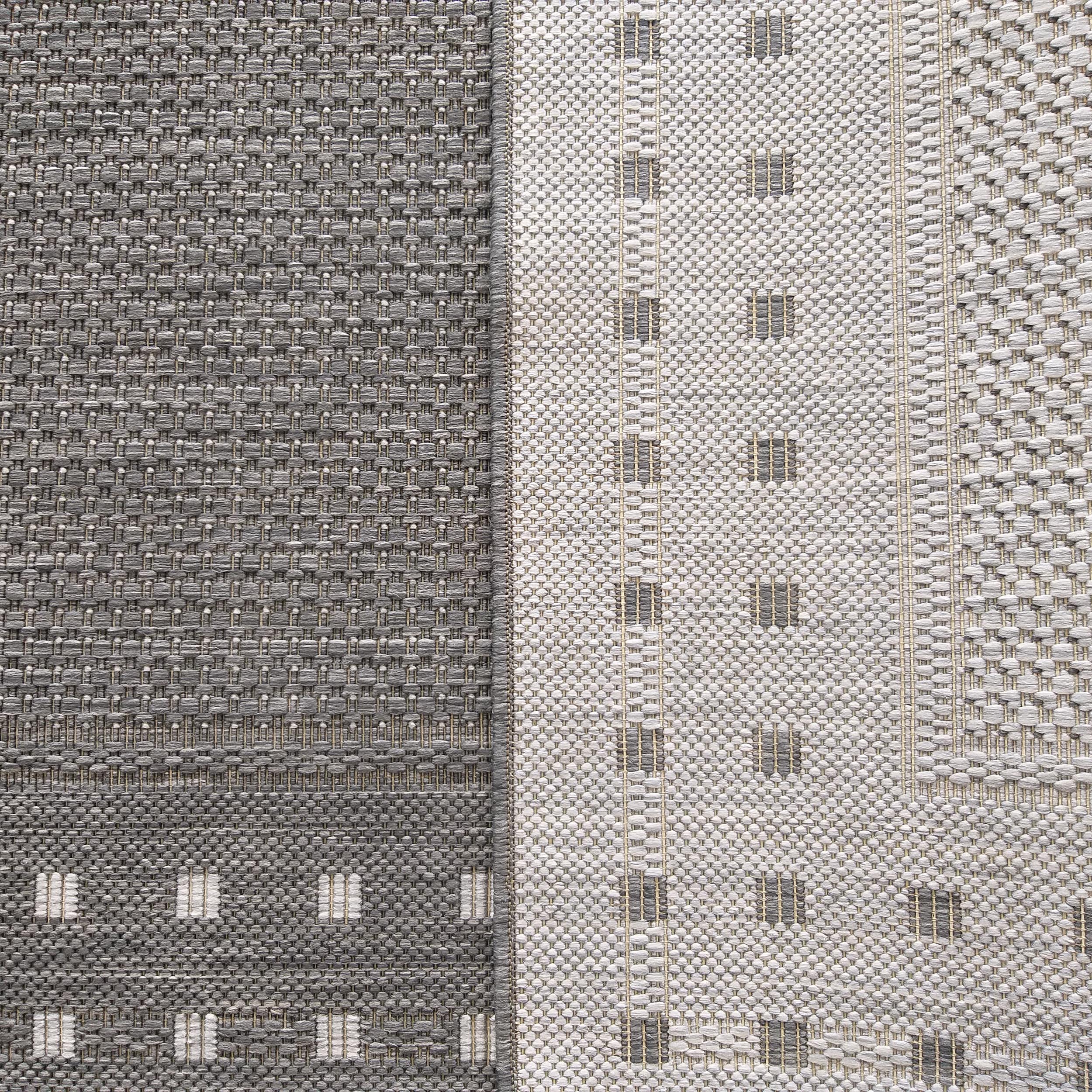 Tapis bicolore en tissage texturé. Une moitié gris foncé avec des carrés clairs, l'autre gris clair avec des lignes sombres, le tout entrelacé de fils beiges
