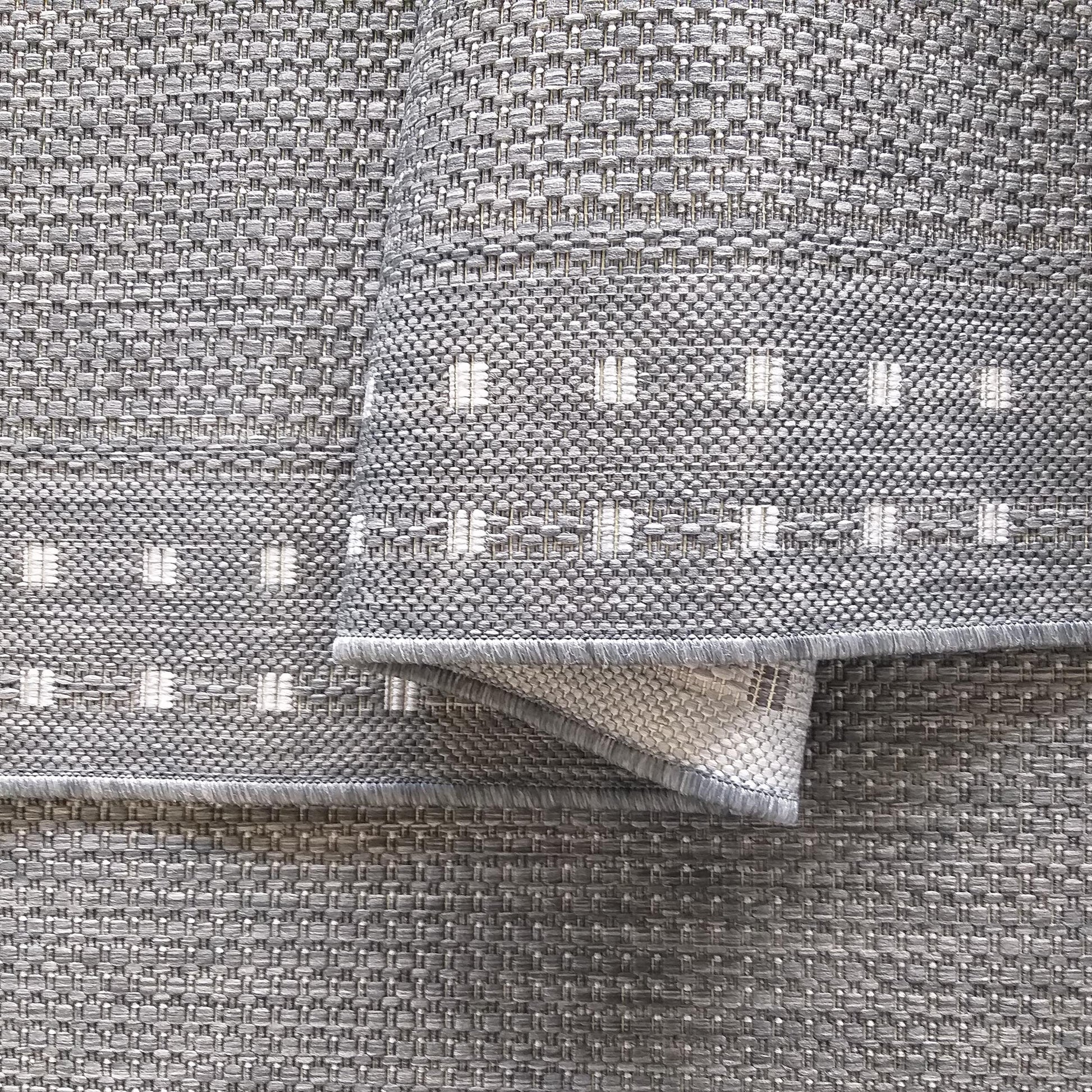 Tapis tissé gris et blanc à la texture épaisse, présentant des bandes horizontales avec des motifs carrés clairs