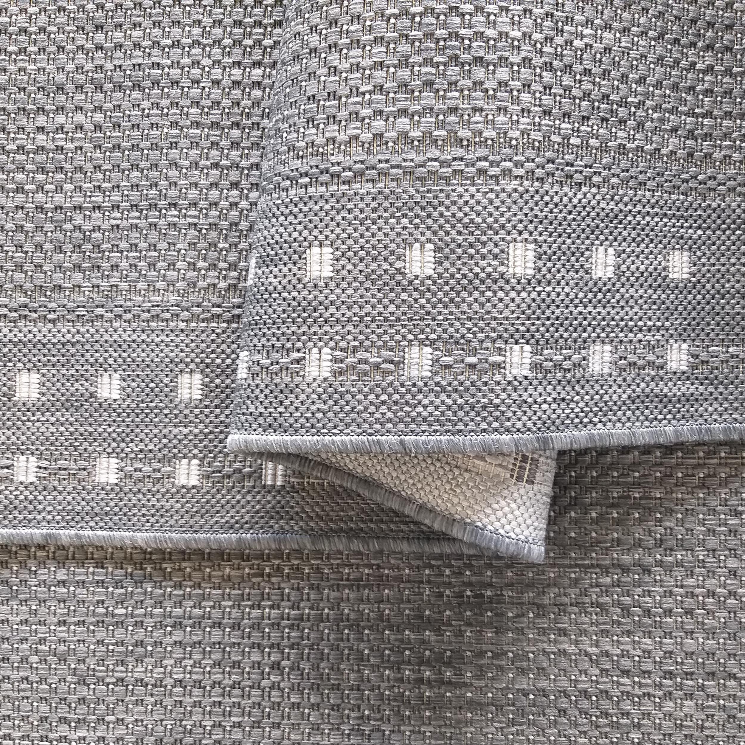 Tapis tissé gris et blanc à la texture épaisse, présentant des bandes horizontales avec des motifs carrés clairs