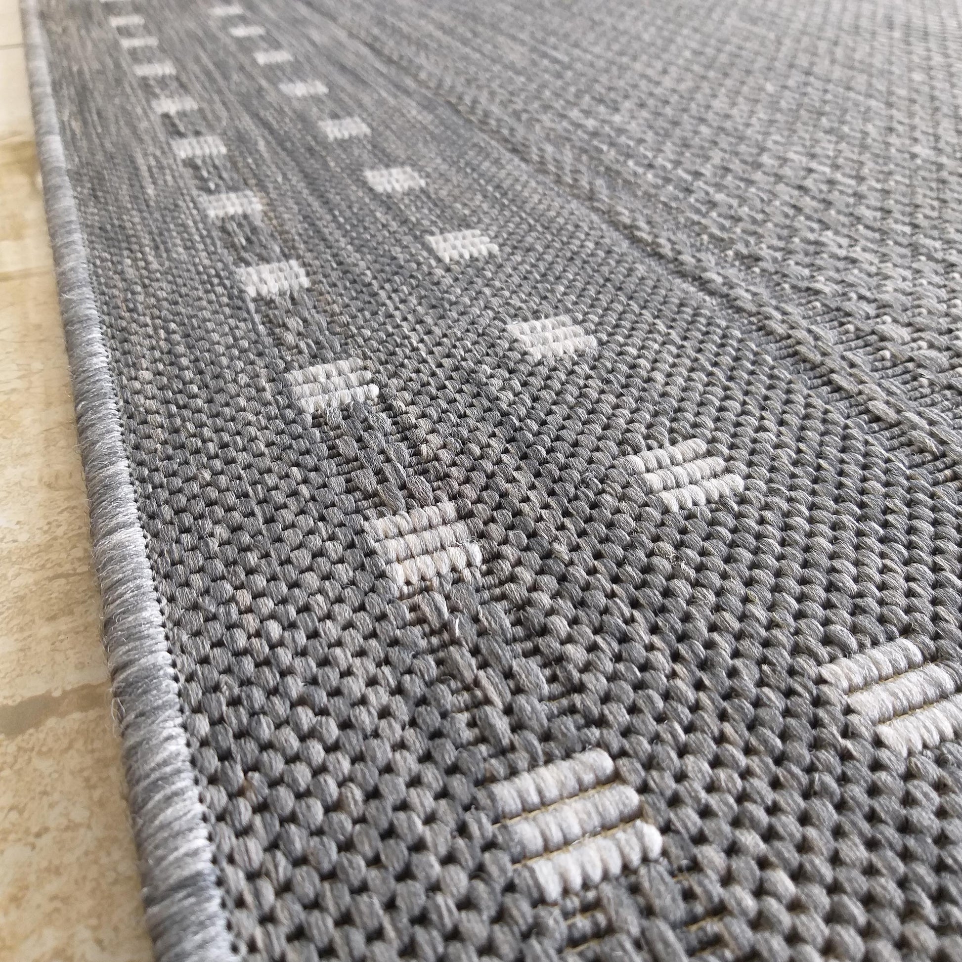 Tapis tissé gris avec des motifs de barres rectangulaires claires en relief sur une texture chinée