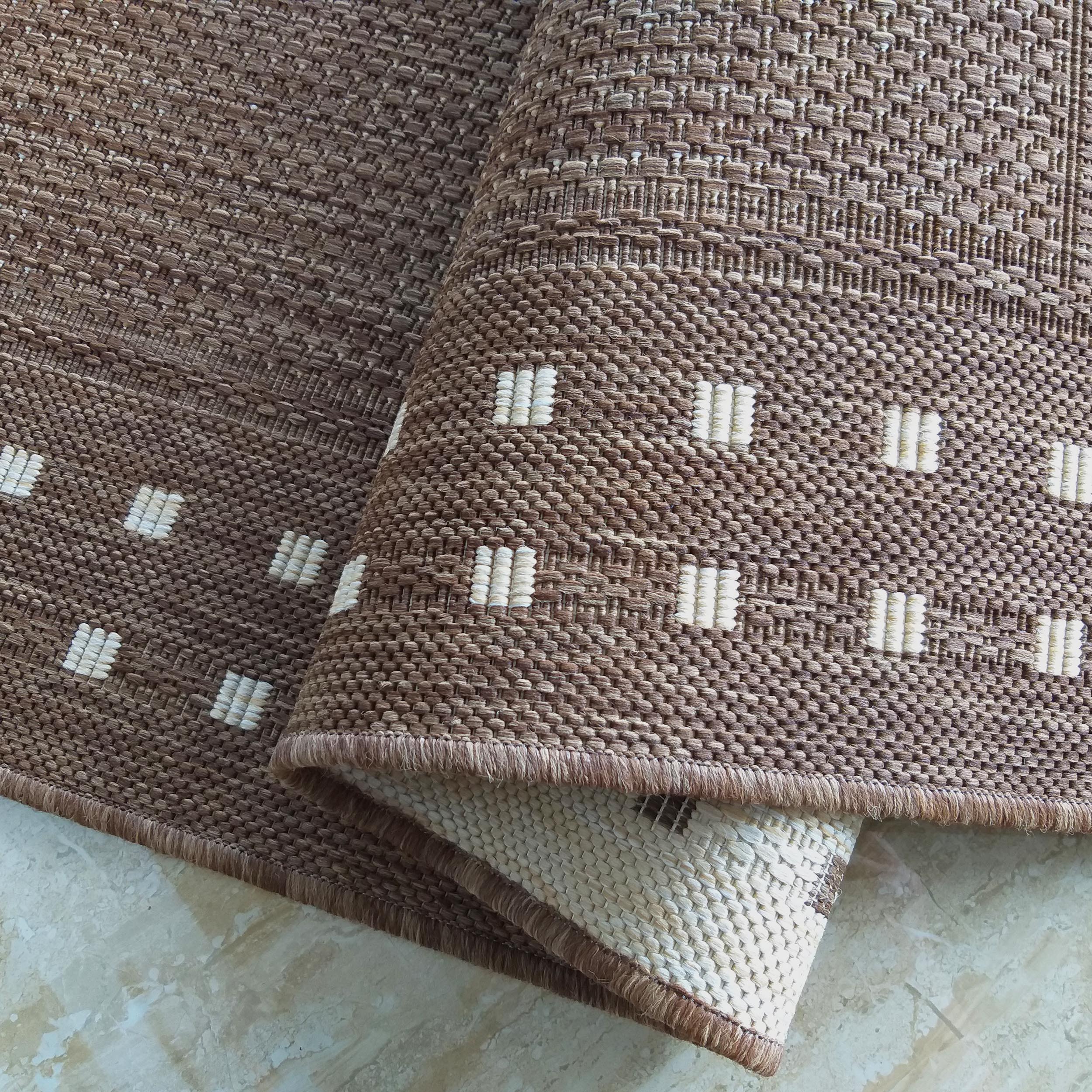 Tapis tissé marron à motifs de barres beige clair, partiellement enroulé sur un sol marbré