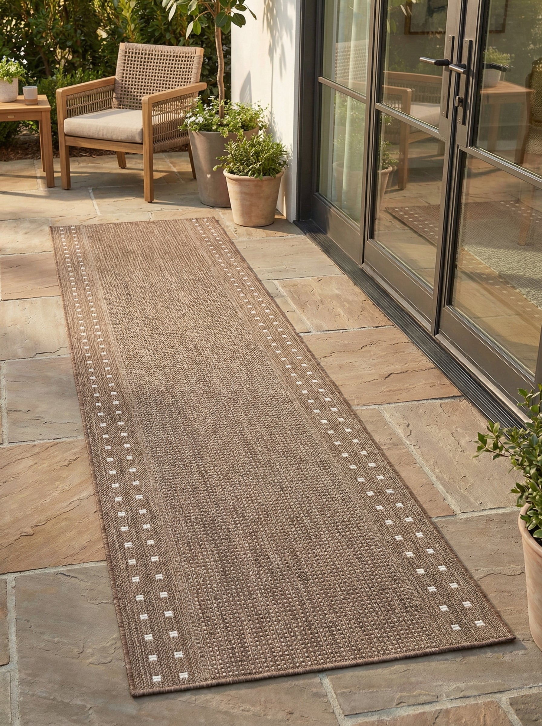 Long tapis en couloir beige chiné, en matière tressée, orné de motifs rectangulaires blancs sur les bords, sur une terrasse