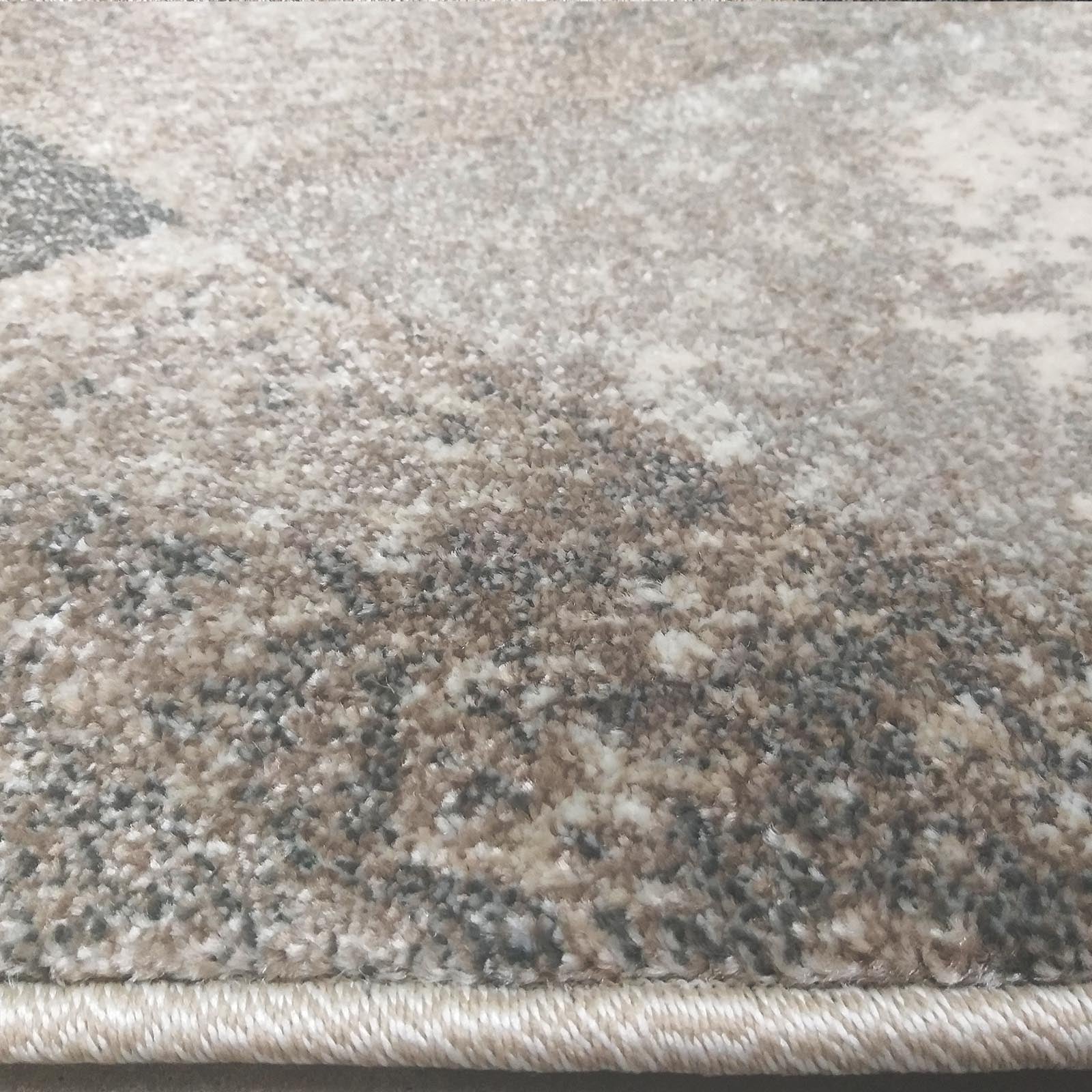 Tapis texturé aux motifs abstraits gris, beige et blanc cassé, avec un bord surpiqué visible