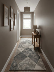 Long tapis aux motifs géométriques de losanges gris clair, gris foncé et crème, certains texturés, posé dans un couloir lumineux