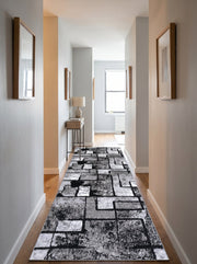 Tapis de couloir noir, gris et blanc à motifs géométriques abstraits texturés sur parquet clair dans un couloir