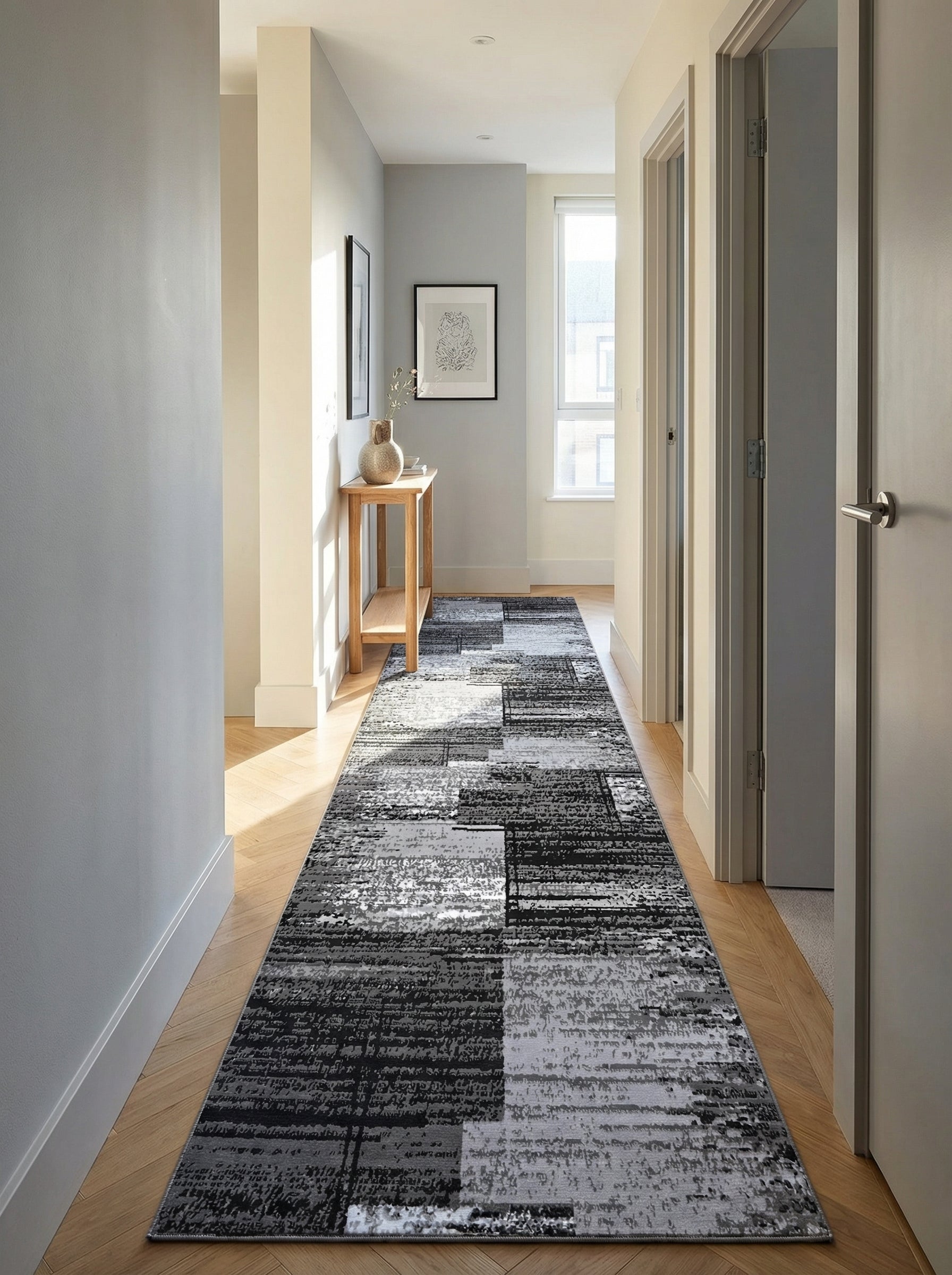Long tapis de couloir noir et gris texturé, à motifs abstraits blocs, posé sur un parquet en chevrons dans un hall lumineux