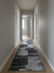 Tapis coureur aux motifs abstraits gris, noirs et blancs, posé sur un parquet clair dans un long couloir lumineux