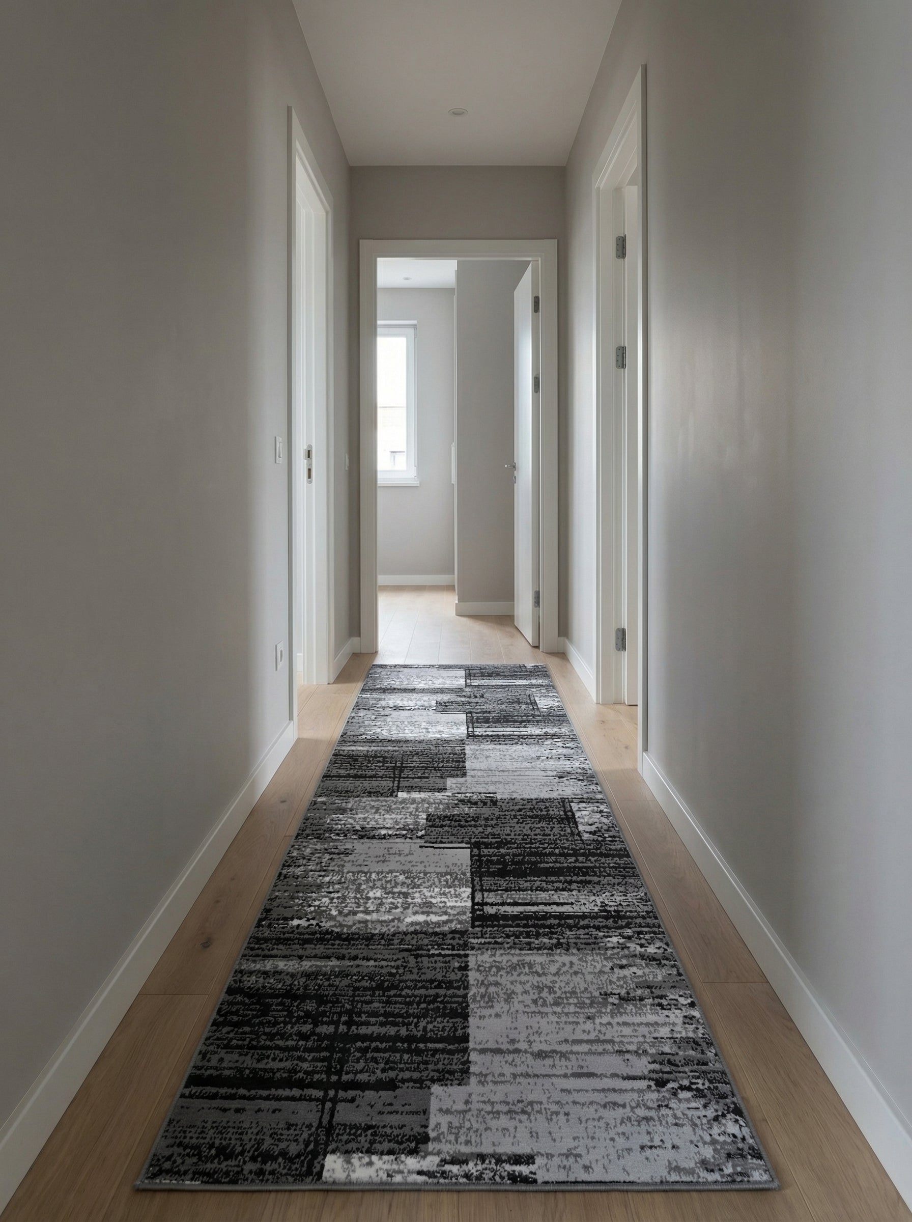 Tapis coureur aux motifs abstraits gris, noirs et blancs, posé sur un parquet clair dans un long couloir lumineux