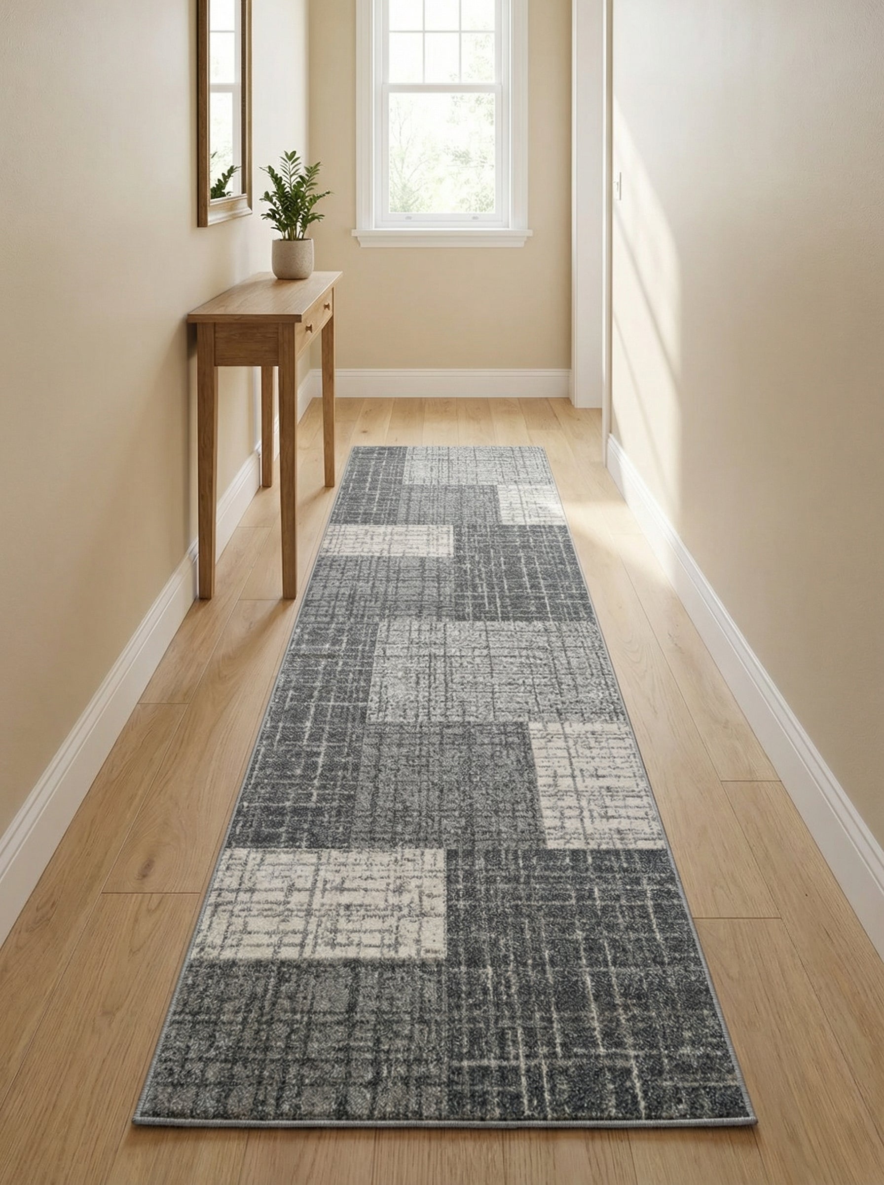 Tapis de couloir rectangulaire aux motifs géométriques abstraits en patchwork de gris foncé, gris clair et beige, posé sur un sol en bois clair dans une entrée