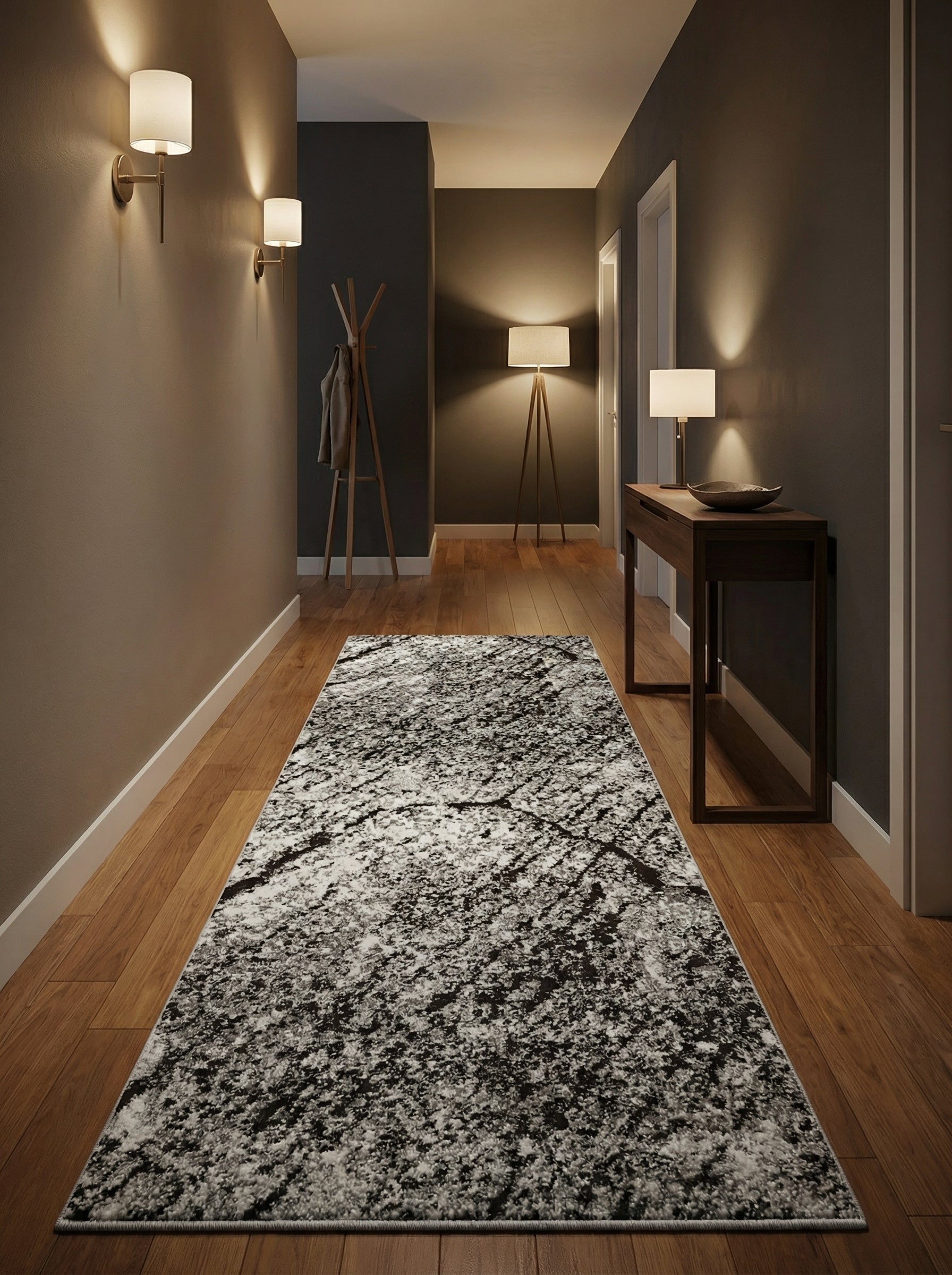 Tapis rectangulaire gris et noir à motif abstrait moucheté et texturé, recouvrant un parquet en bois dans un couloir d'entrée illuminé