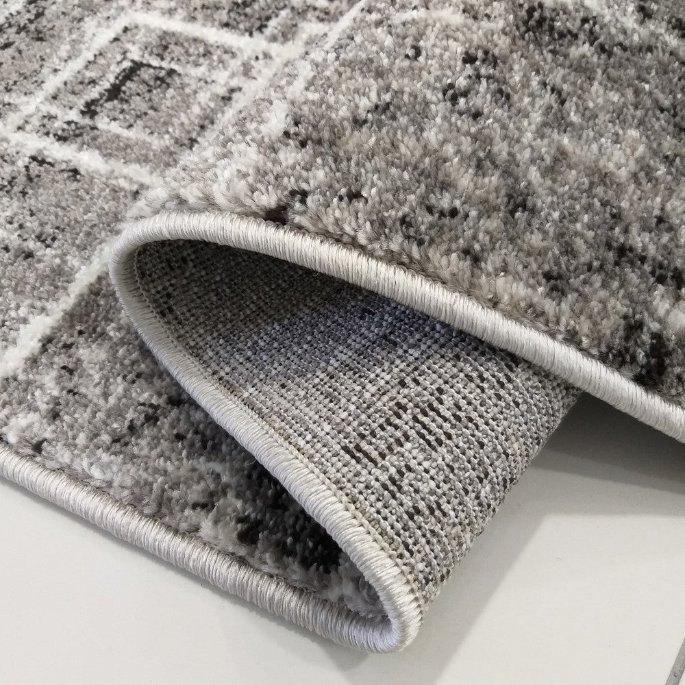 Gros plan sur un tapis gris, blanc et noir avec un motif géométrique abstrait, montrant sa texture poilue et son revers tissé