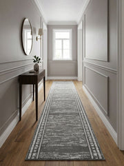 Long tapis gris aux motifs abstraits et délavés, avec bordures géométriques blanches et noires, sur un parquet clair d'un couloir