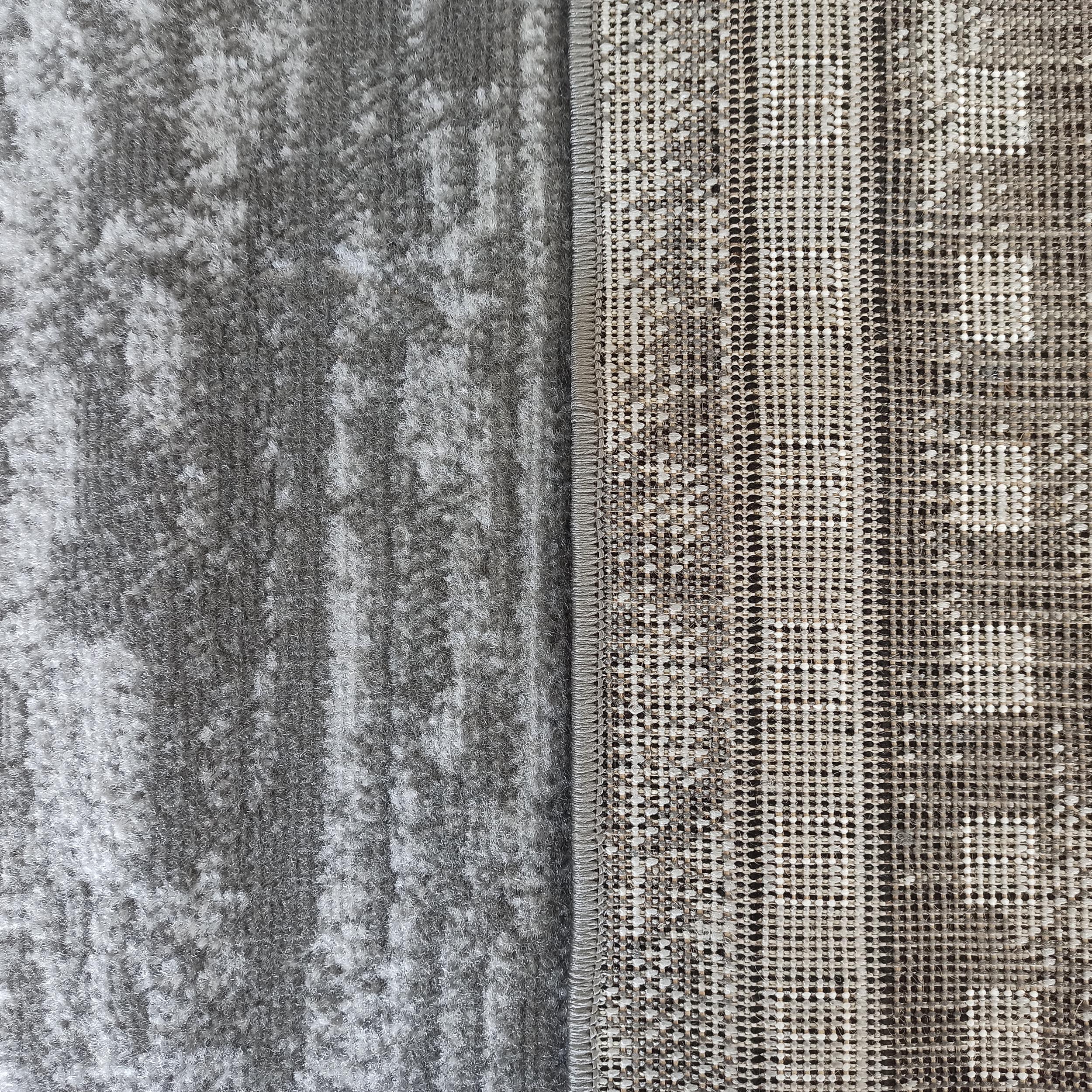 Tapis bicolore gris et blanc, avec une partie à poils longs et une autre montrant le tissage quadrillé de son envers