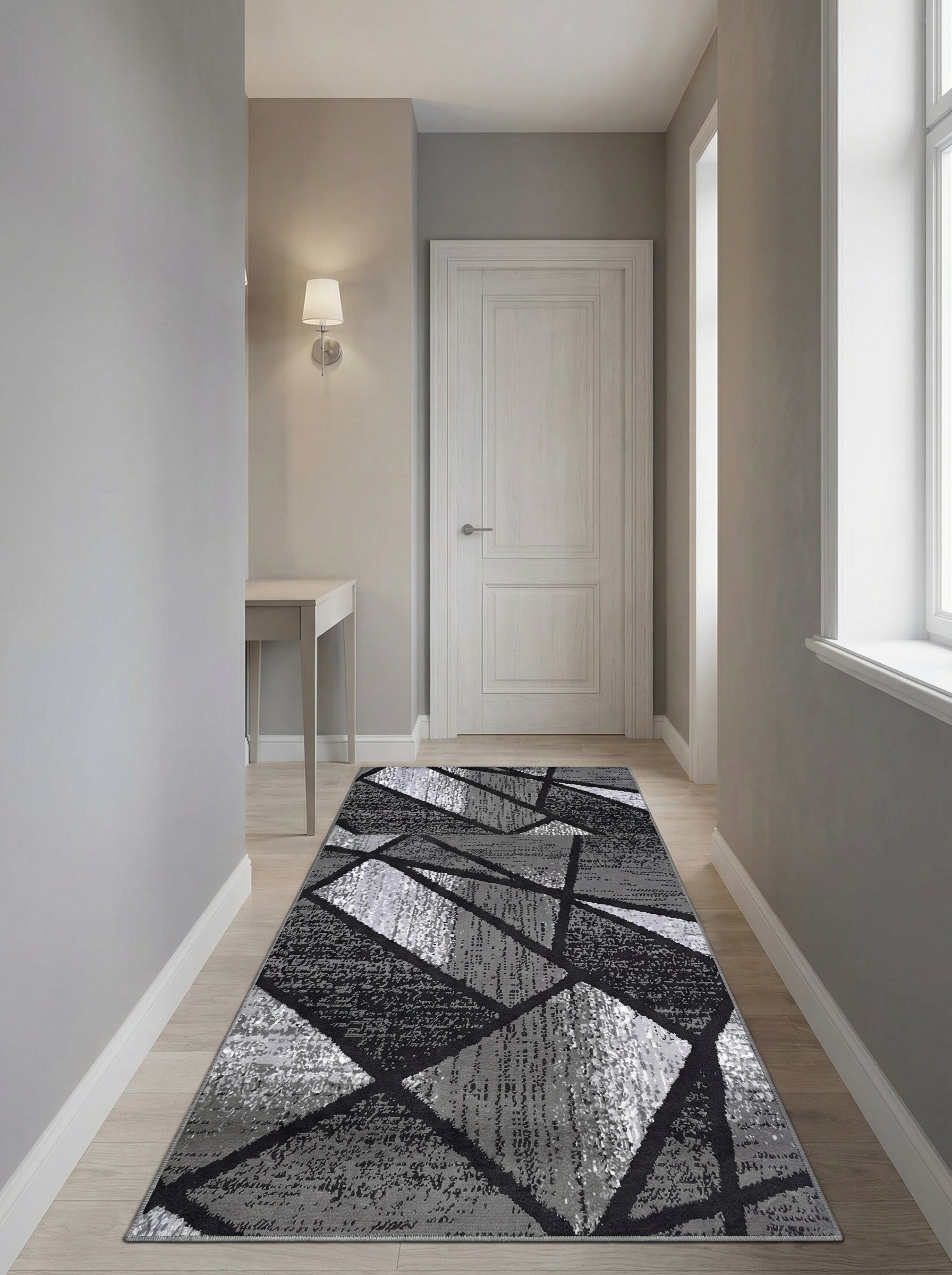 Grand tapis de couloir aux motifs géométriques abstraits gris, noirs et blancs, sur un sol en bois clair dans une entrée