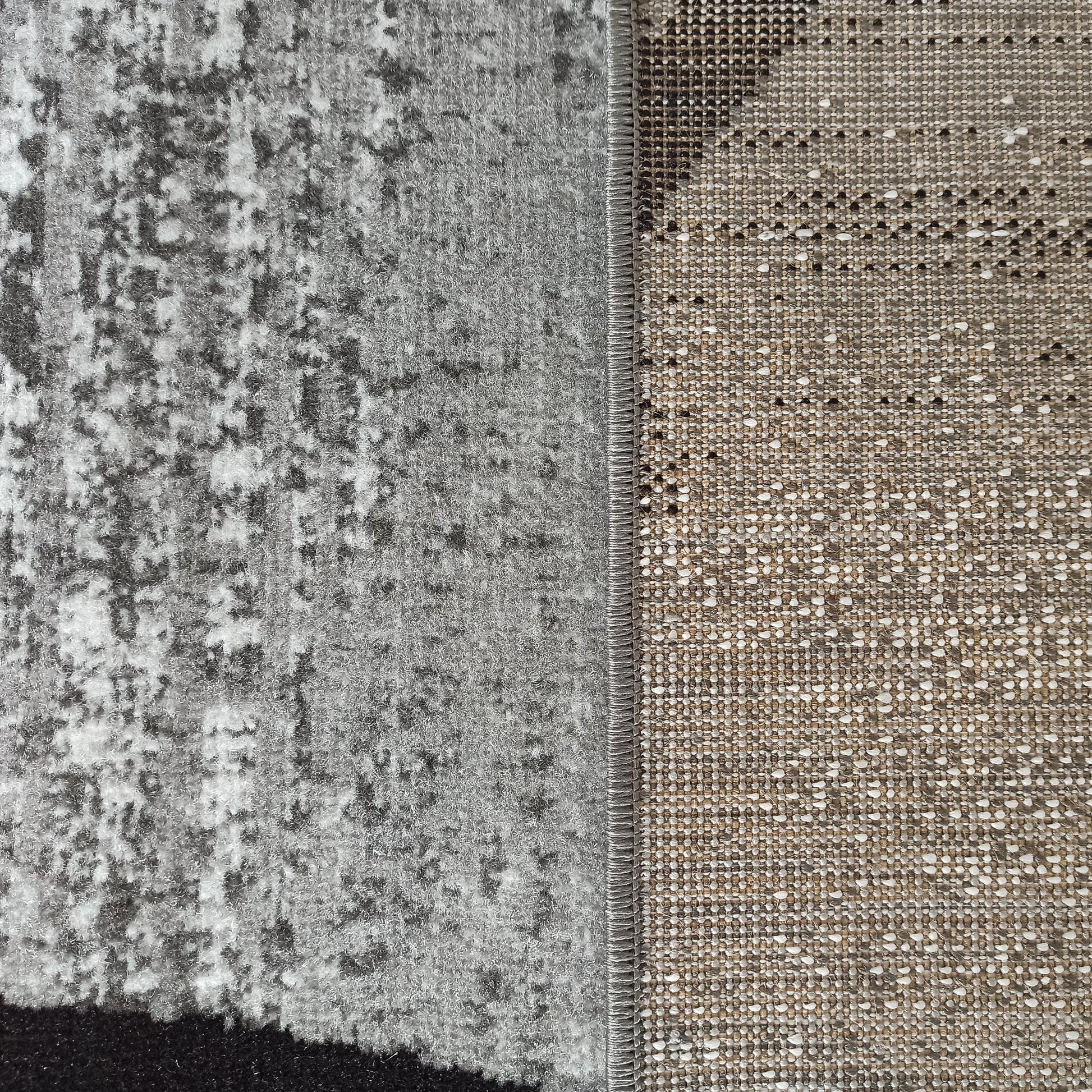 Tapis à poil court gris clair et foncé aux motifs abstraits, bordé d'un revers tissé beige moucheté de blanc et noir