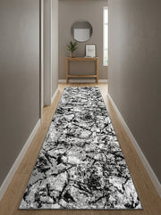 Tapis de couloir rectangulaire à motifs abstraits noirs, gris et blancs, posé sur un parquet dans une entrée lumineuse